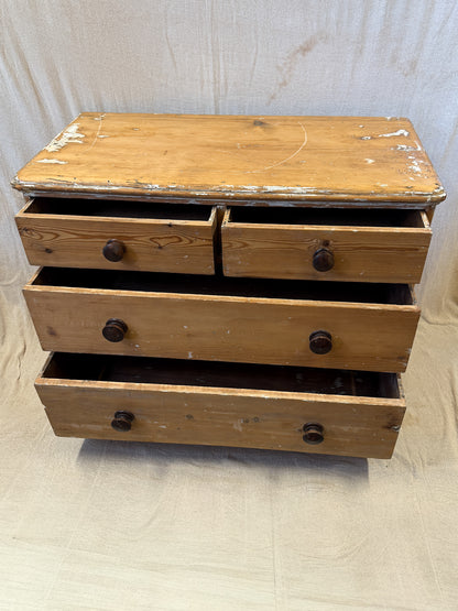 A rustic wooden chest of drawers with a distressed finish, featuring a top surface and three drawers with dark round knobs, set against a light fabric backdrop.