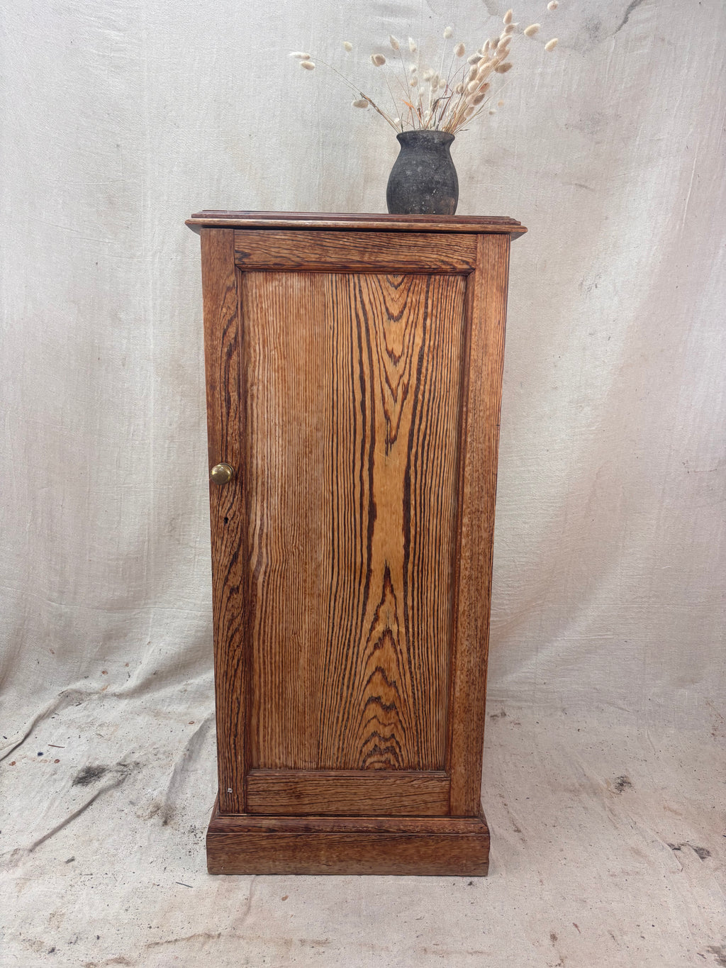 Wooden cabinet with a vase of dried flowers on a textured white background