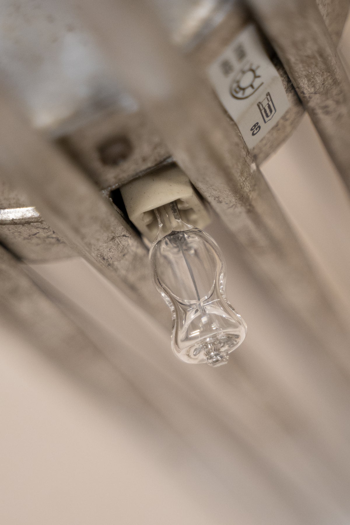A close-up shot of a clear glass radiant panel light bulb mounted on a metal radiator, with a white plastic connector and a temperature sensor nearby.