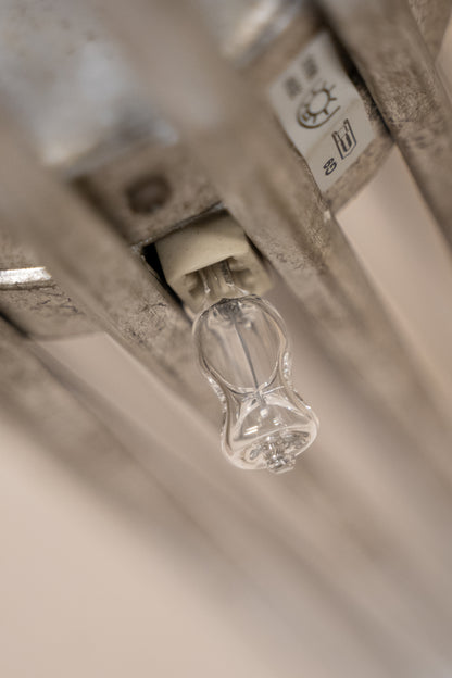 A close-up shot of a clear glass radiant panel light bulb mounted on a metal radiator, with a white plastic connector and a temperature sensor nearby.