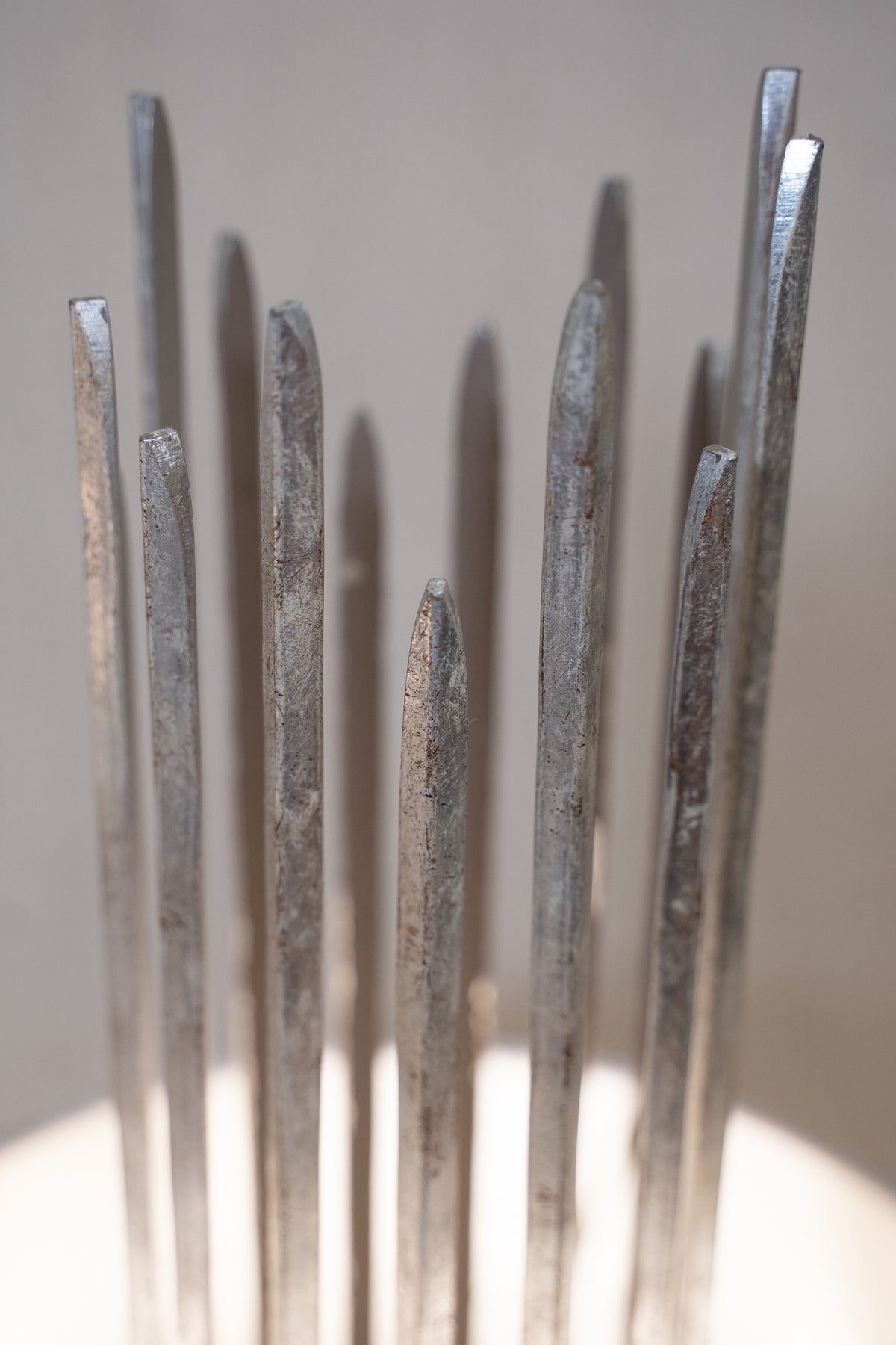 A close-up of several tall, slender metallic rods or pins with a brushed silver-gray finish, standing upright against a soft neutral background.