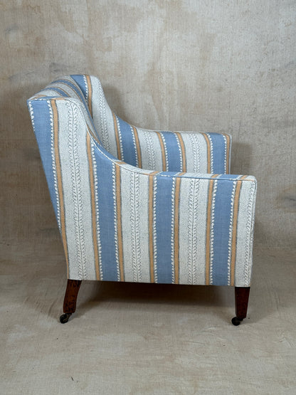 A vintage-style wingback armchair upholstered in a vertical striped fabric with blue, beige, and off-white patterns, featuring dark wood legs with casters, set against a textured beige studio backdrop.