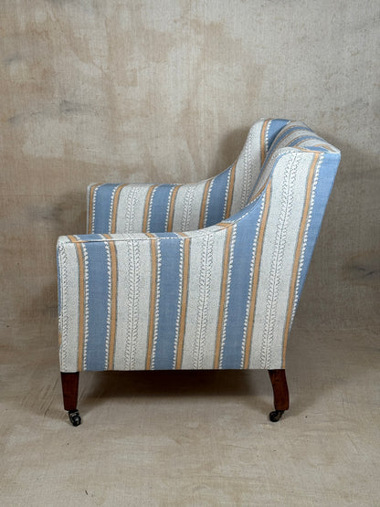 A single upholstered armchair shown from the side against a textured beige studio backdrop. The chair has a striped fabric pattern with vertical bands of light blue, off-white, tan, and cream, plus small white geometric motifs.
