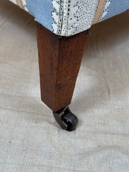 Close-up of a wooden upholstered furniture leg with a dark metal caster wheel, resting on a light beige fabric surface.