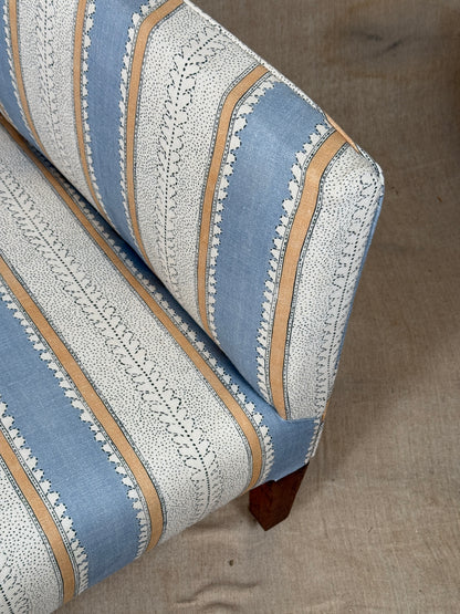 Close-up of an upholstered armchair corner showing a striped fabric pattern with light blue, white, and tan vertical bands, set against a neutral beige floor.