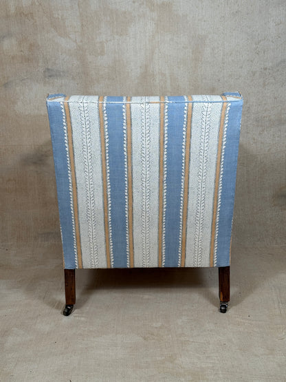 A vintage upholstered armchair viewed from the back, featuring vertical stripes in light blue, cream, and tan on a beige textured studio background.