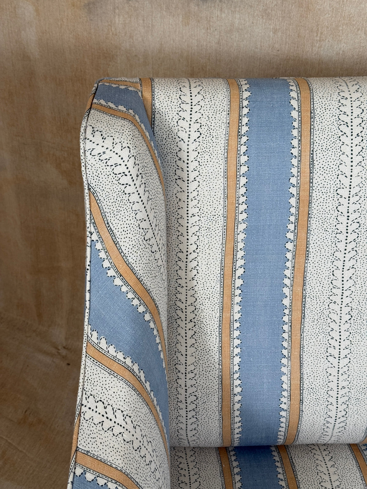 A close-up of upholstered furniture showing a striped fabric pattern with light blue, off-white, and tan vertical bands, set against a warm beige wall.