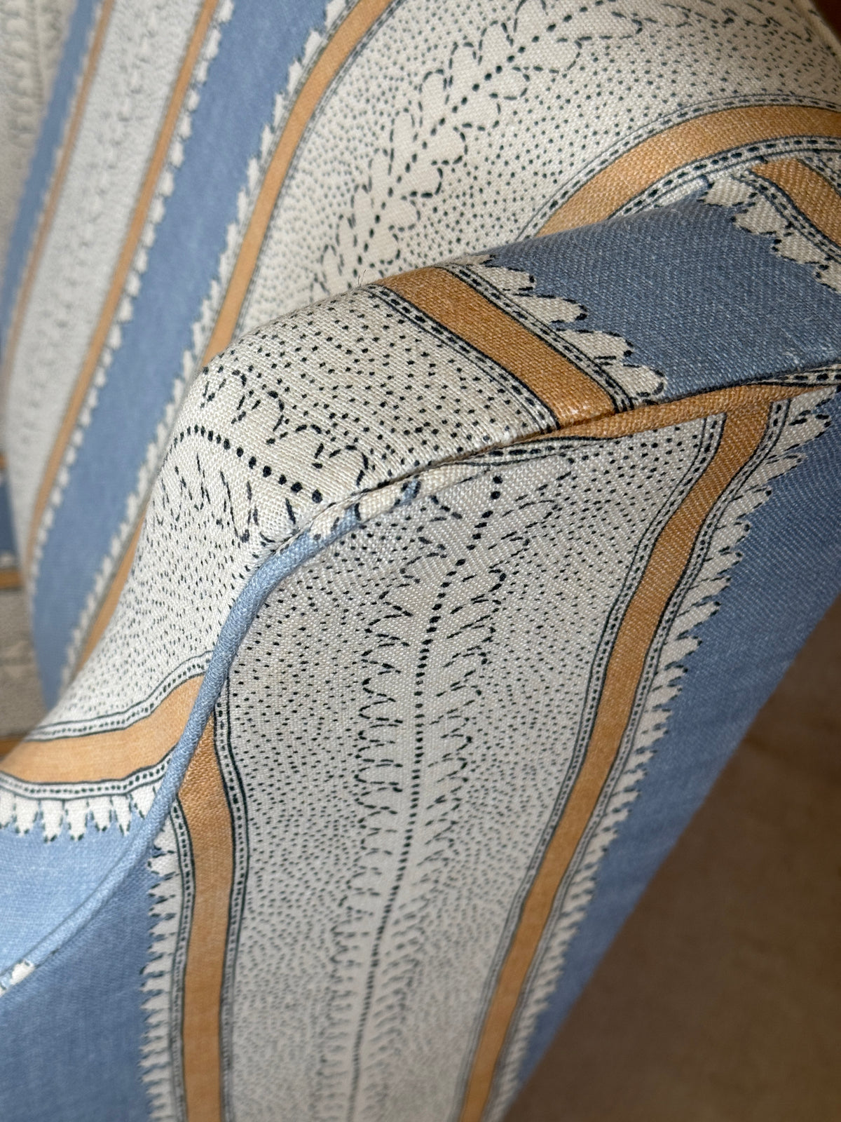 Close-up of patterned upholstery fabric with a cream base, blue sections, and tan stripes with black dotted and embroidered detailing.
