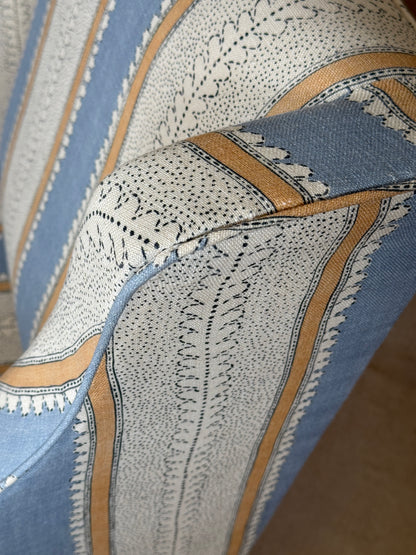 Close-up of patterned upholstery fabric with a cream base, blue sections, and tan stripes with black dotted and embroidered detailing.