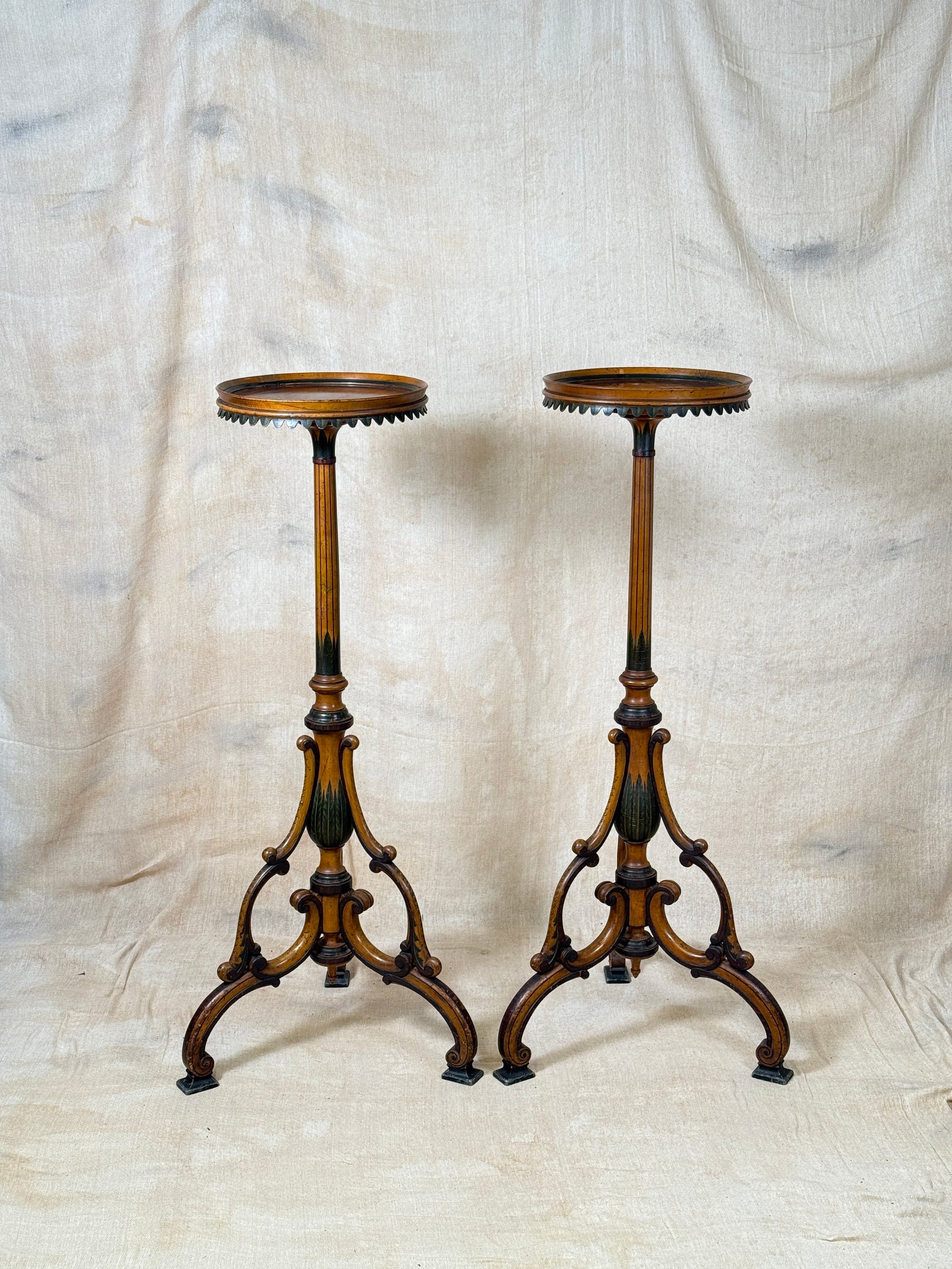 Two ornate dark brown Torchere Stands with decorative scrollwork bases, shown against a draped beige fabric backdrop. 