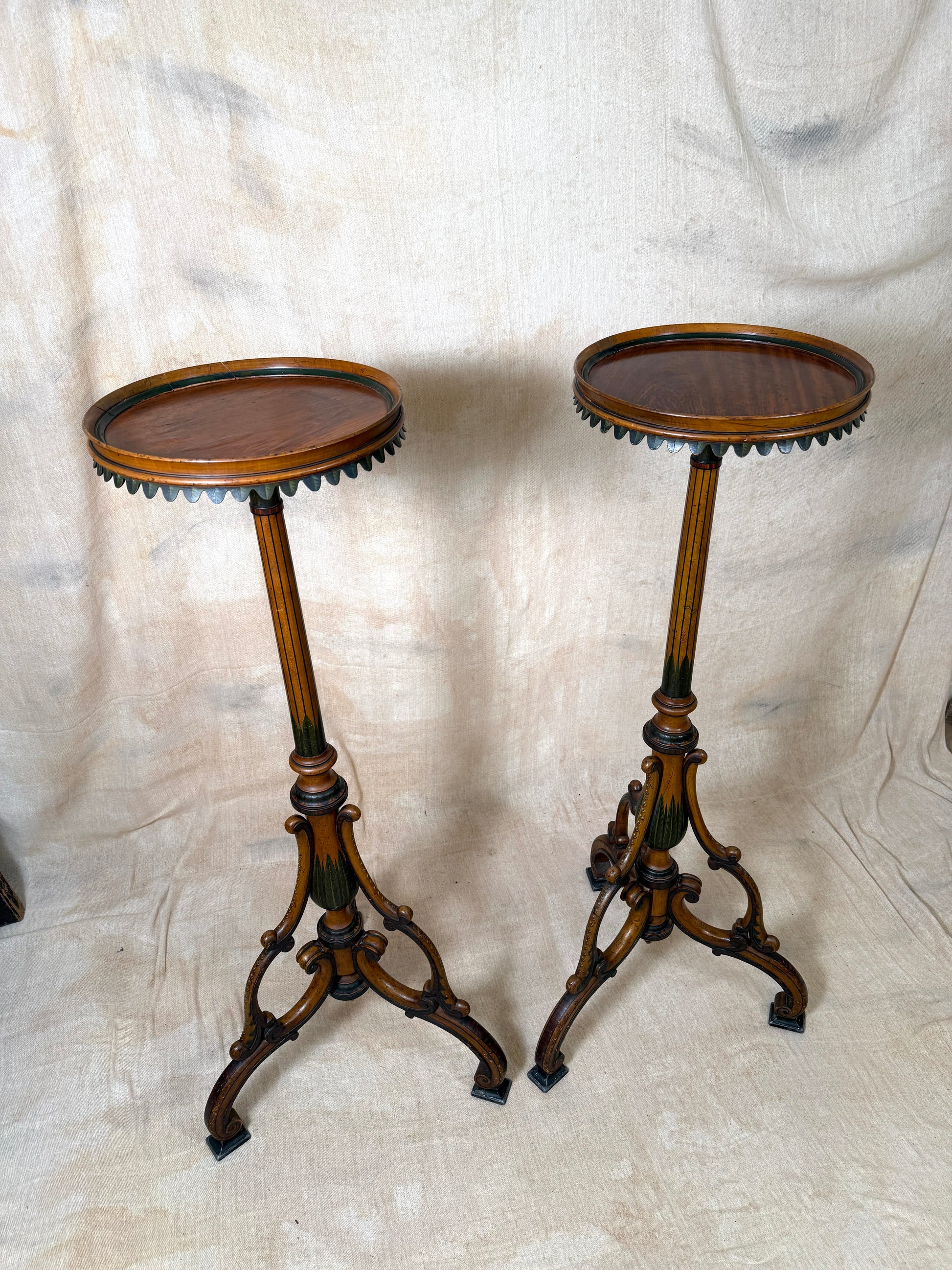 Two ornate dark brown Torchere Stands with decorative scrollwork bases, shown against a draped beige fabric backdrop. 