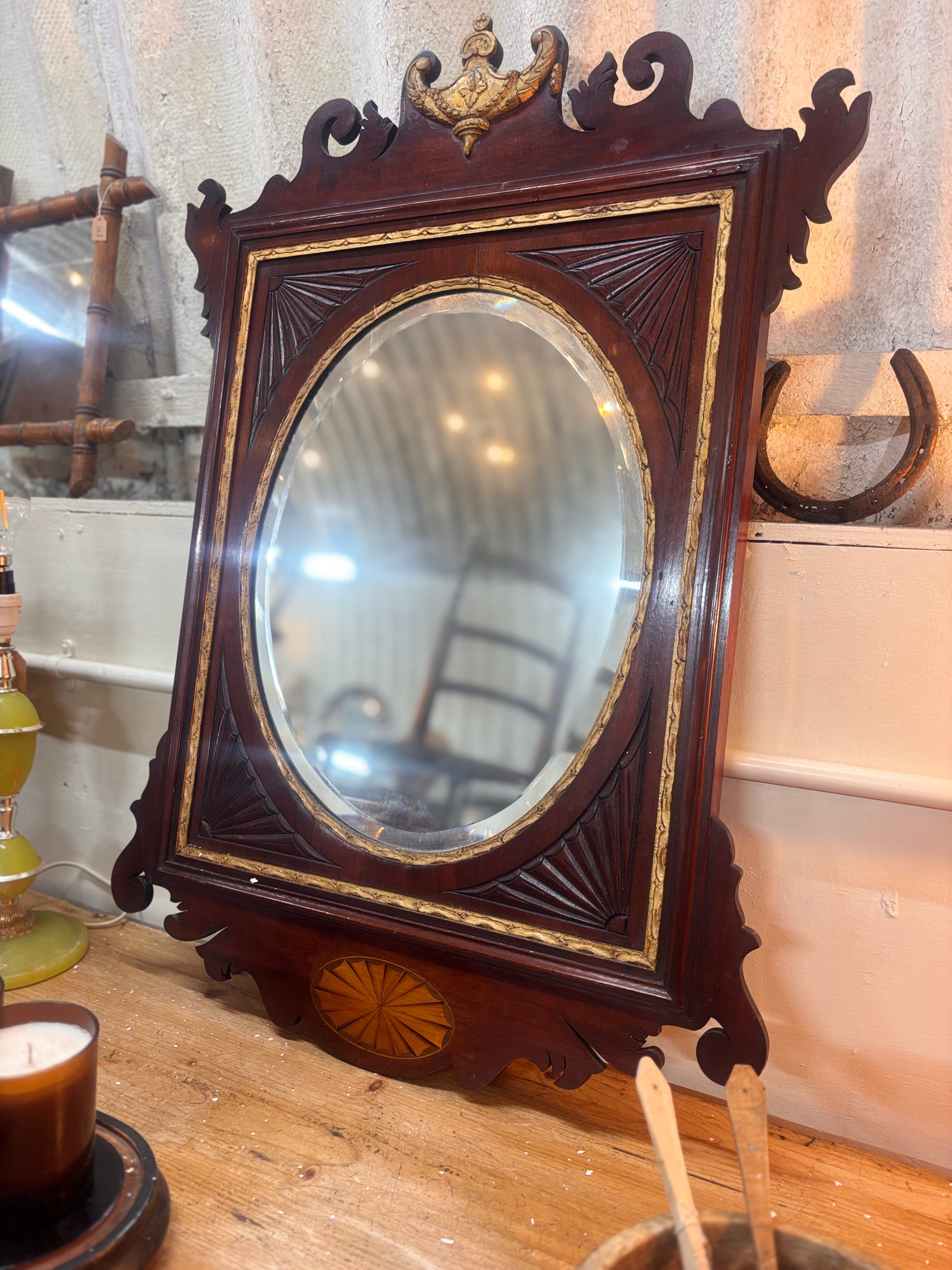Chippendale revival mahogany mirror with gilded urn crest, carved fretwork, and oval plate in a rectangular frame