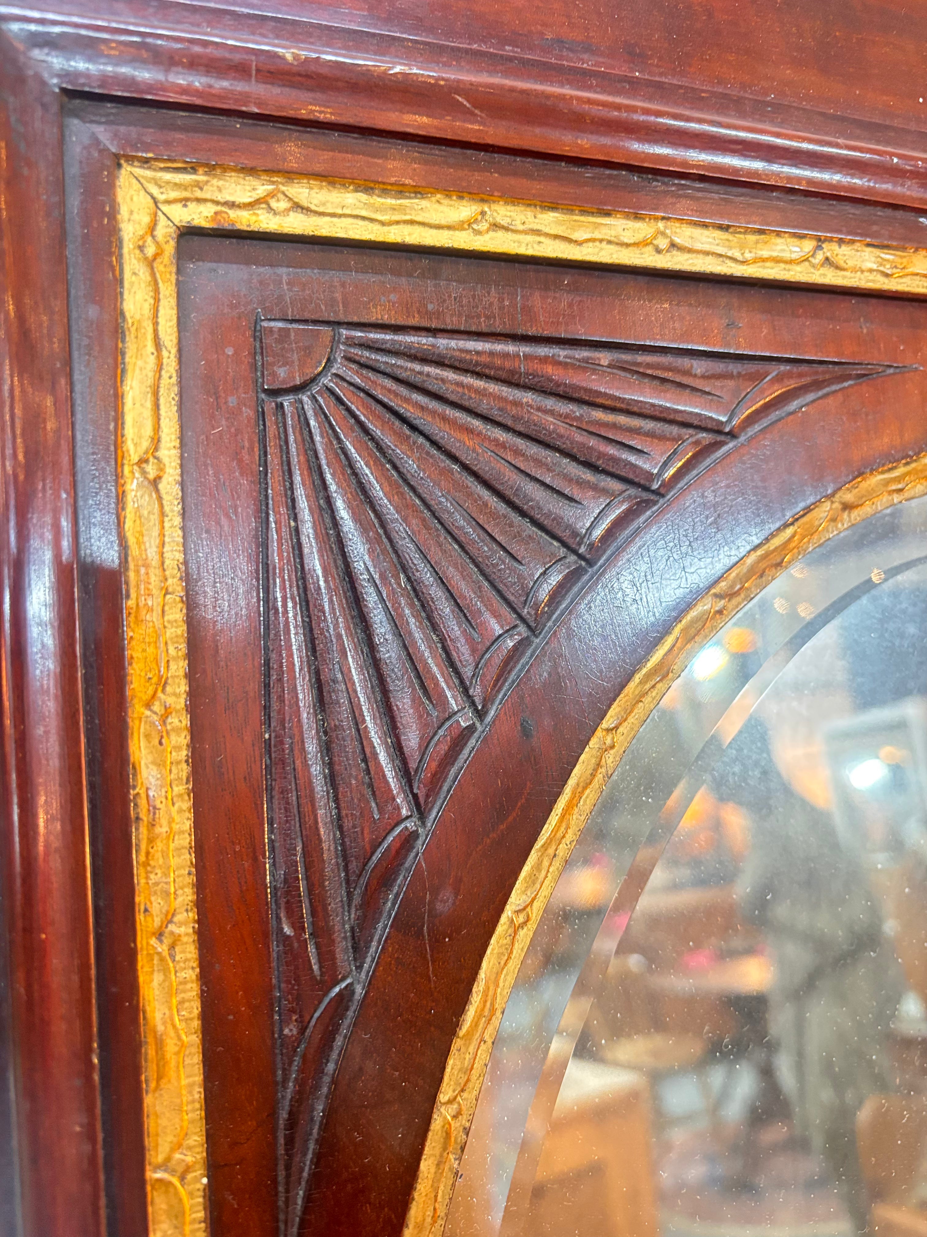 Corner detail of Chippendale revival mahogany mirror with gilded urn crest, carved fretwork, and oval plate in a rectangular frame