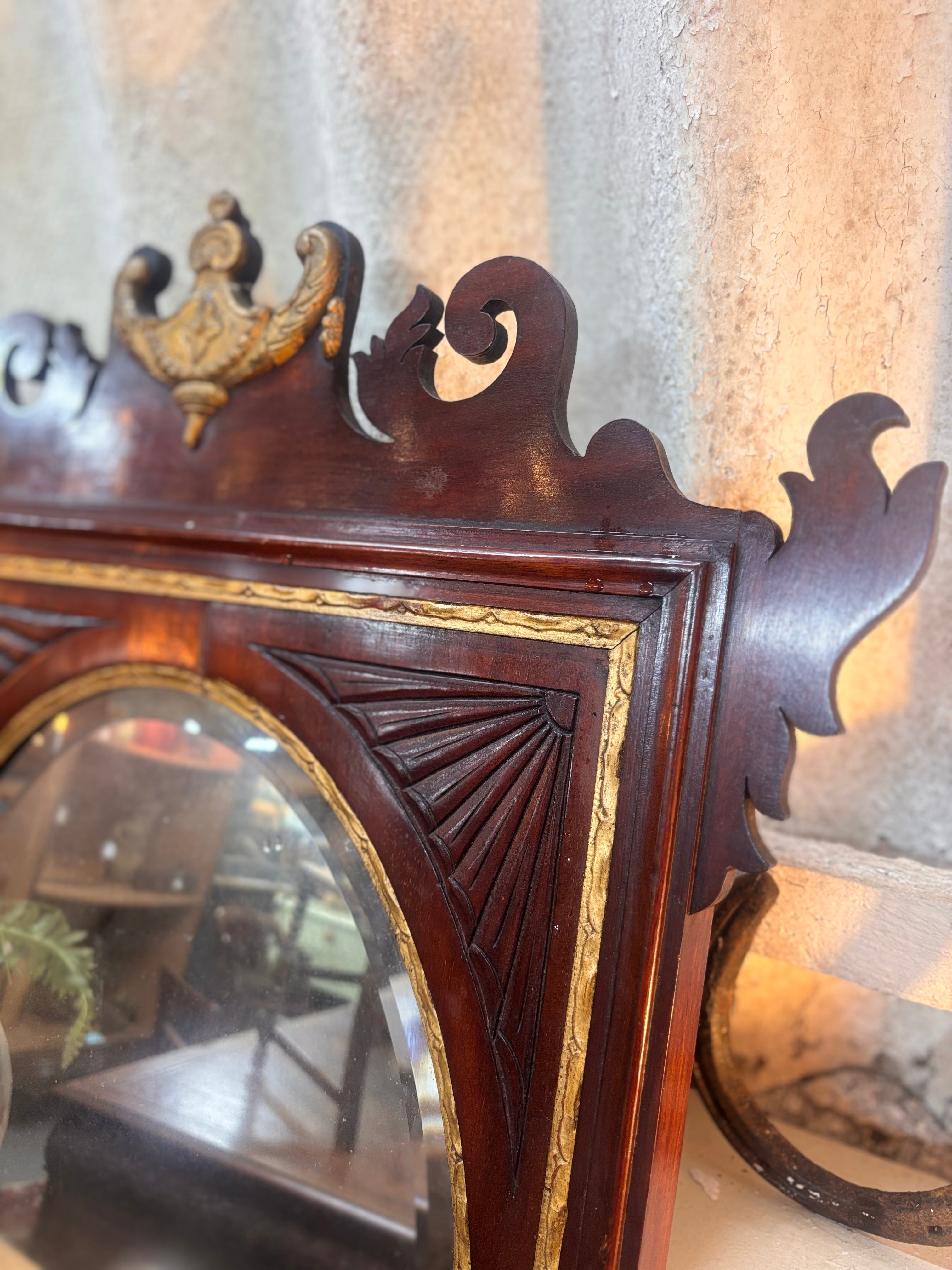 Chippendale revival mahogany mirror with gilded urn crest, carved fretwork, and oval plate in a rectangular frame