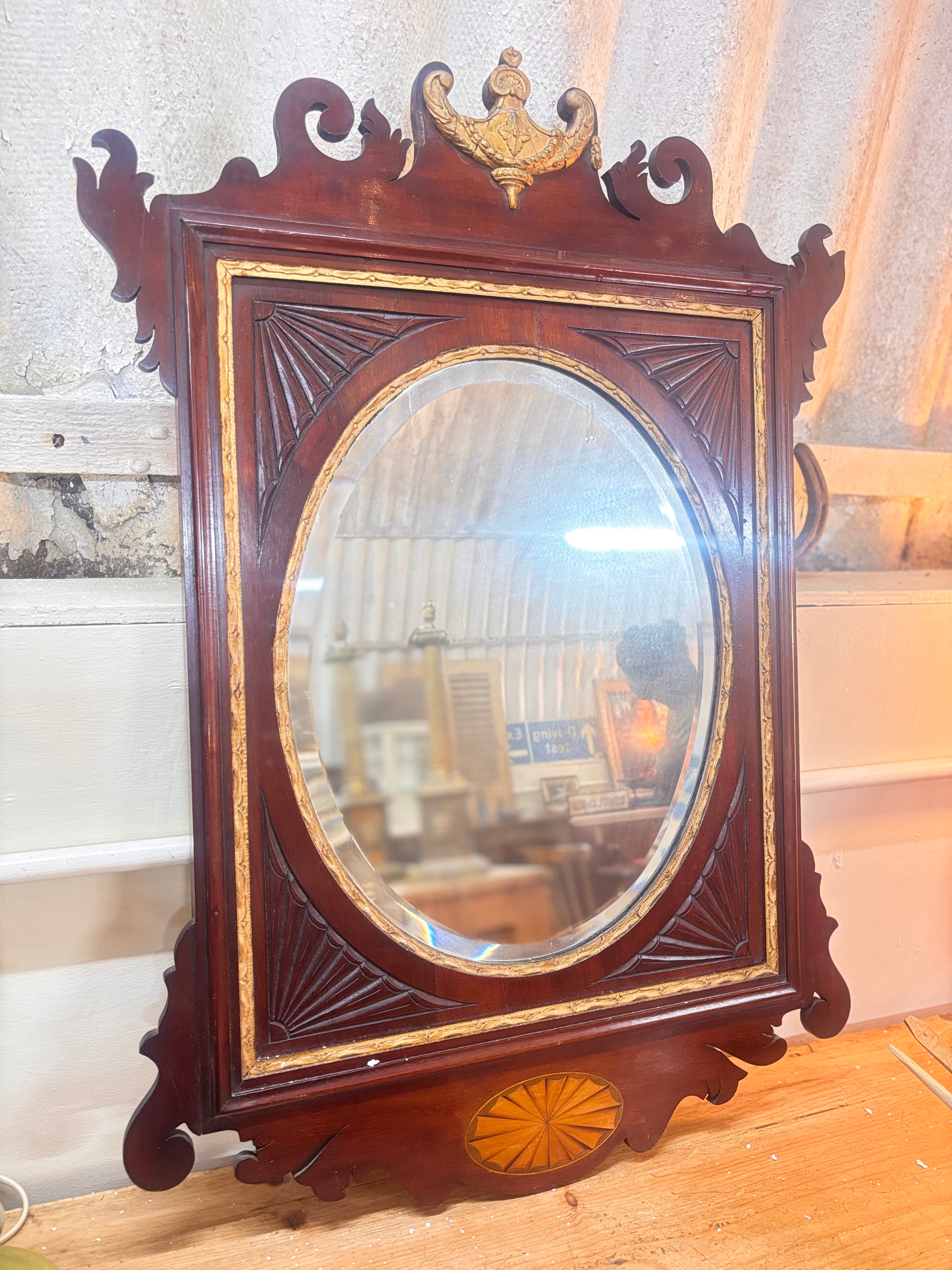 Chippendale revival mahogany mirror with gilded urn crest, carved fretwork, and oval plate in a rectangular frame