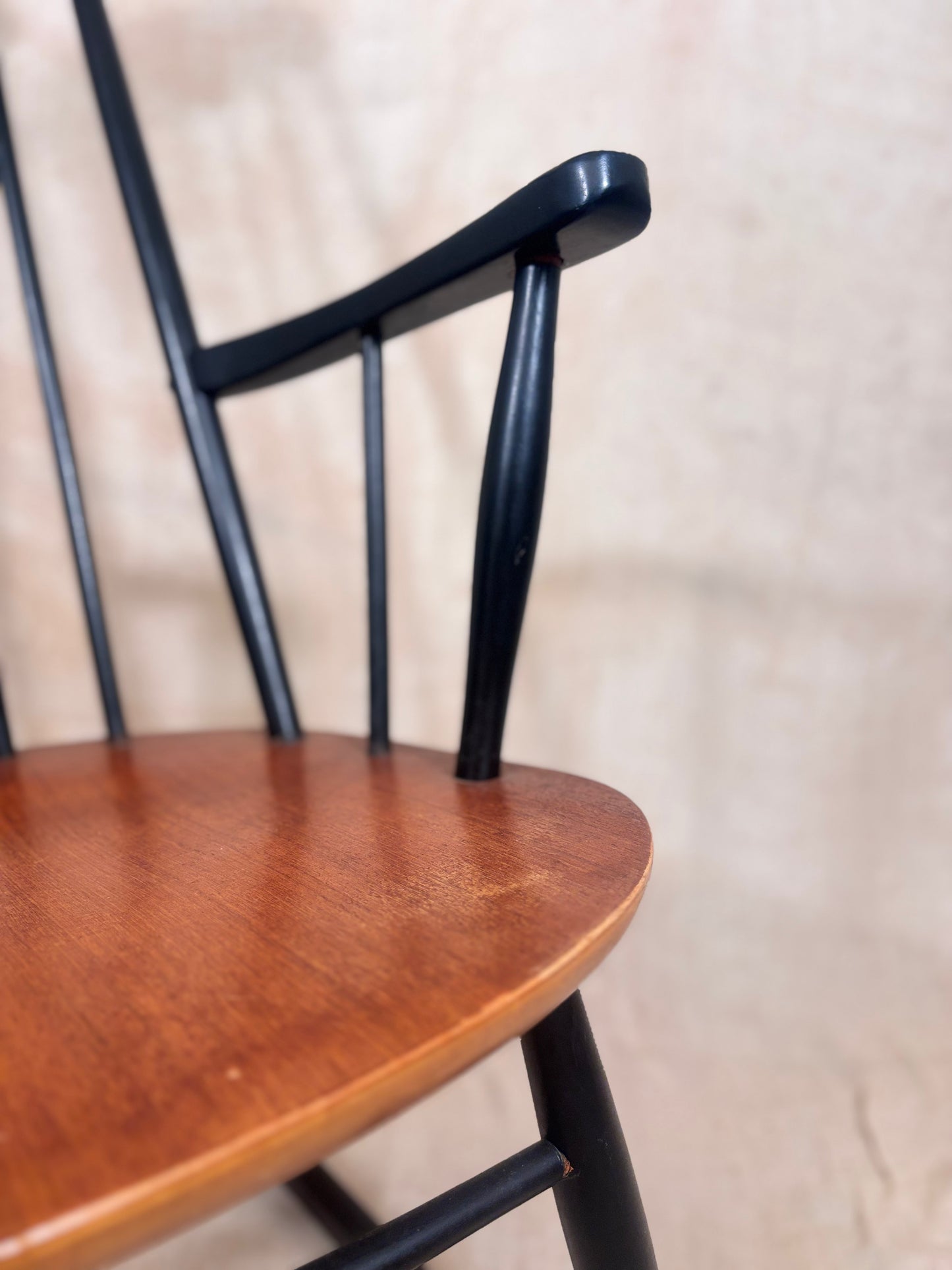 Close-up detail of a wooden chair showing a warm medium-brown wood seat and a glossy black metal frame with curved armrests and vertical spindles.