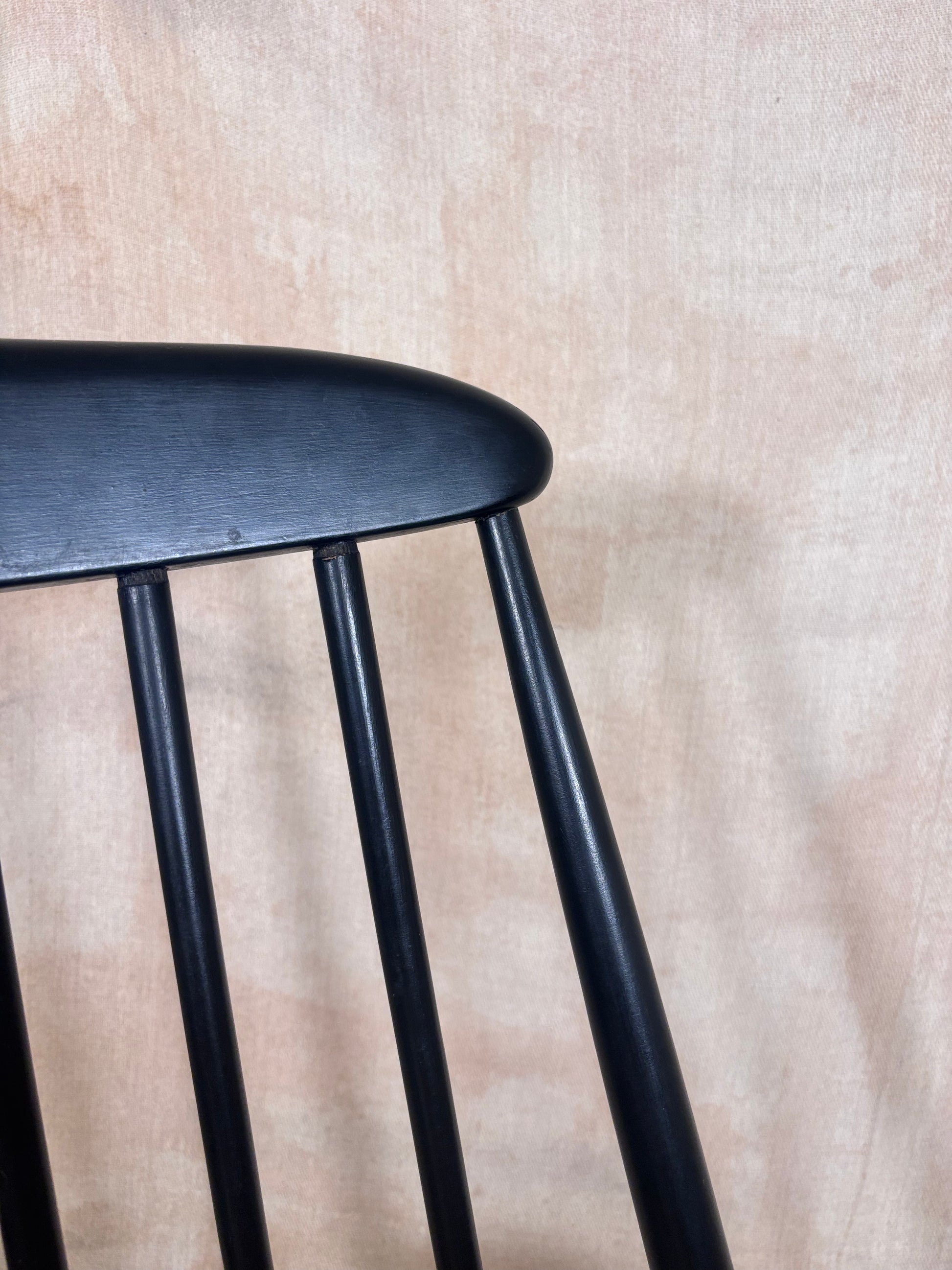 Close-up of a black wooden chair back with a curved top and vertical spindles, set against a textured beige wall.