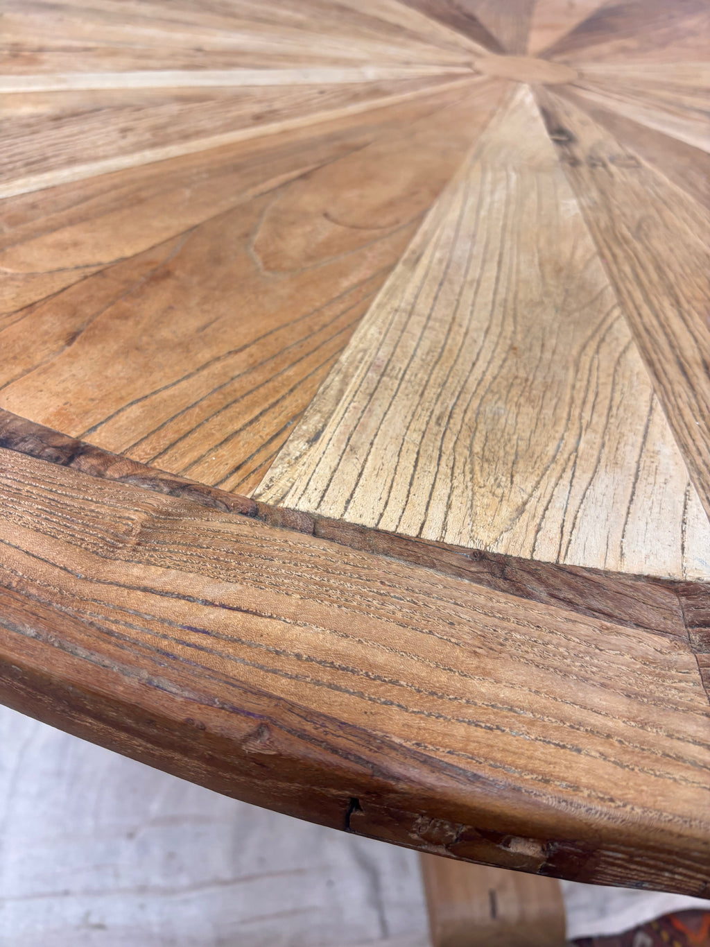 Rustic round wooden pedestal dining table with sunburst-patterned top and cross-leg base, photographed against a neutral backdrop.