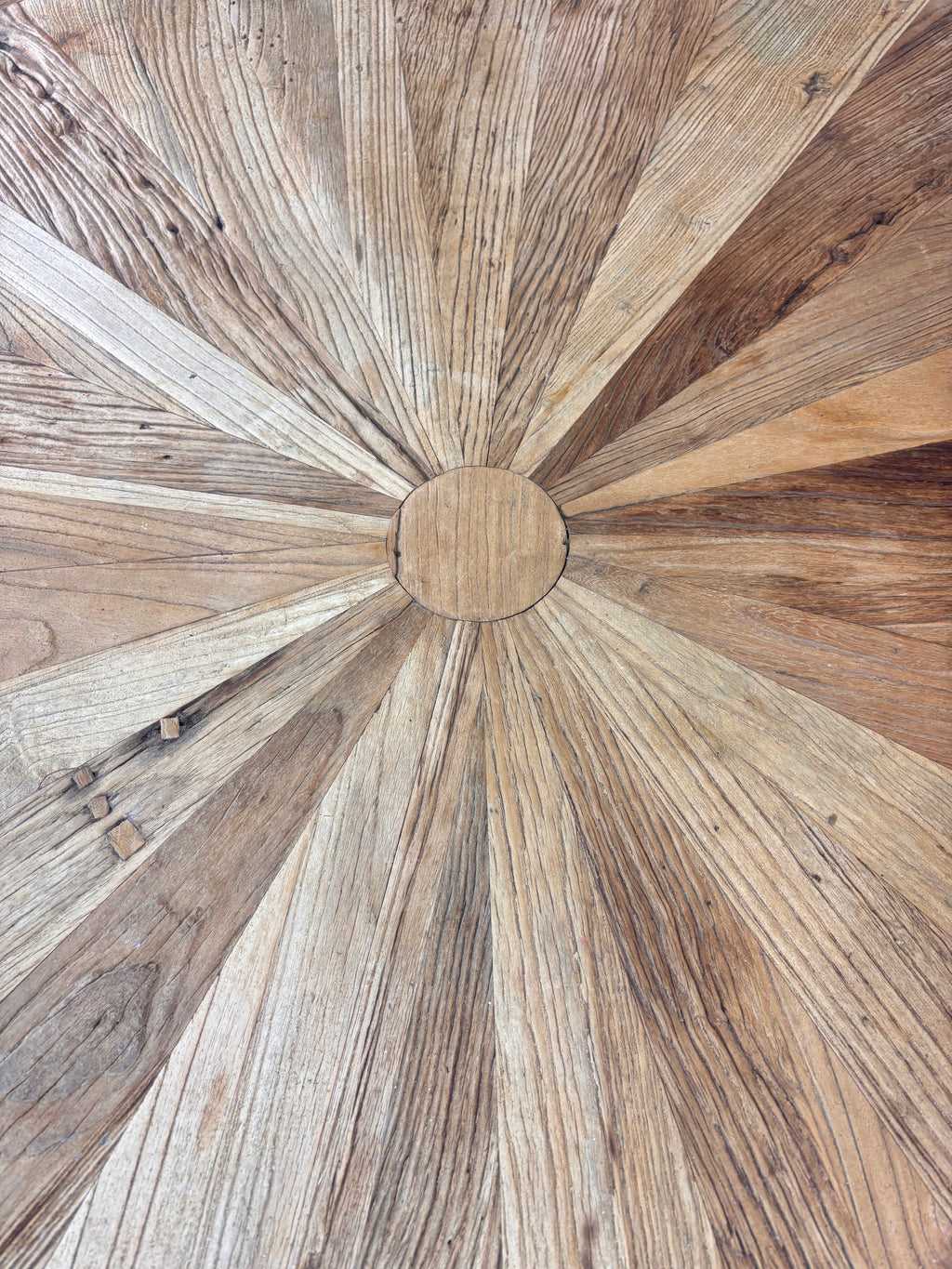 Rustic round wooden pedestal dining table with sunburst-patterned top and cross-leg base, photographed against a neutral backdrop.