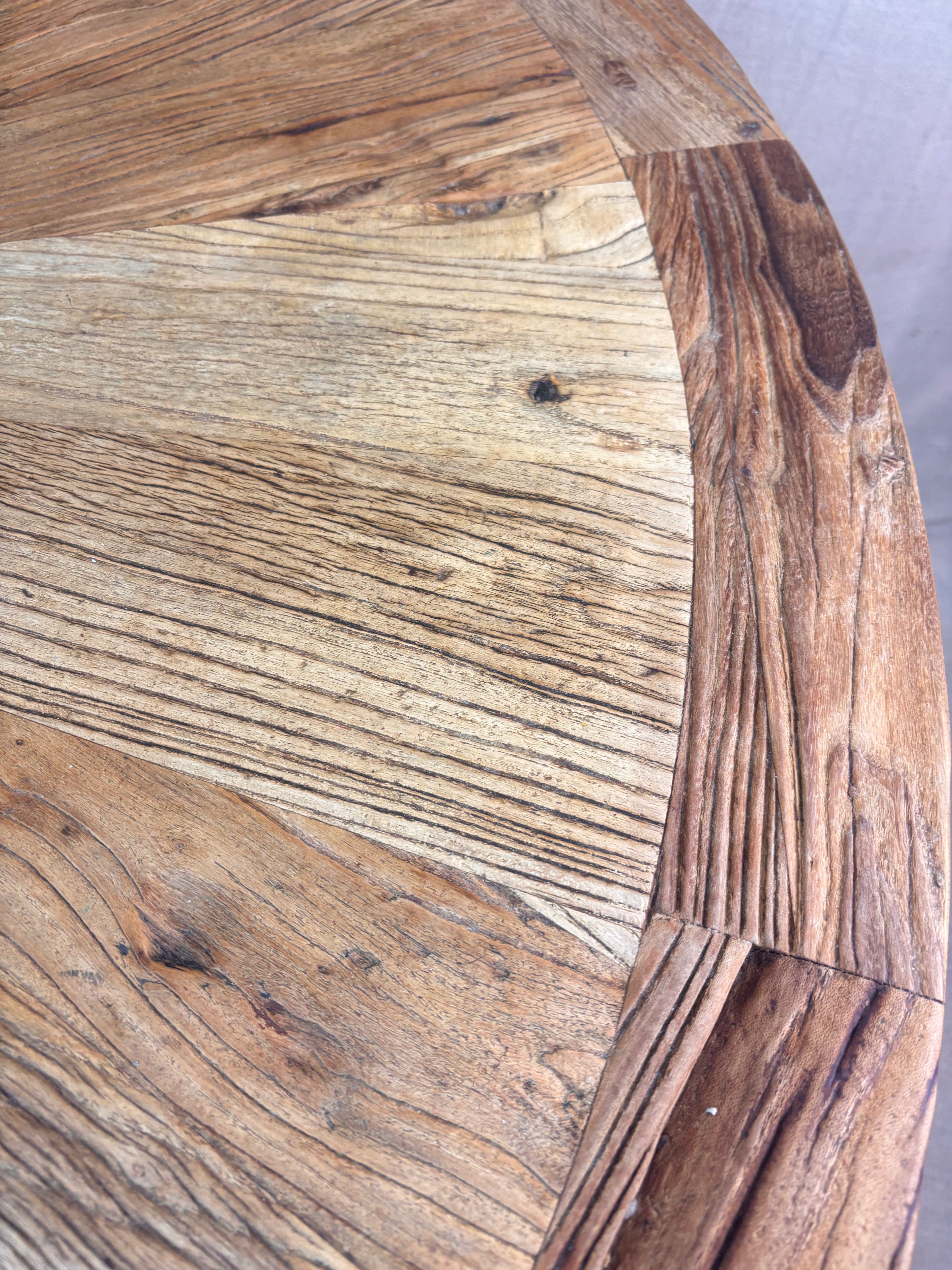 Rustic round wooden pedestal dining table with sunburst-patterned top and cross-leg base, photographed against a neutral backdrop.