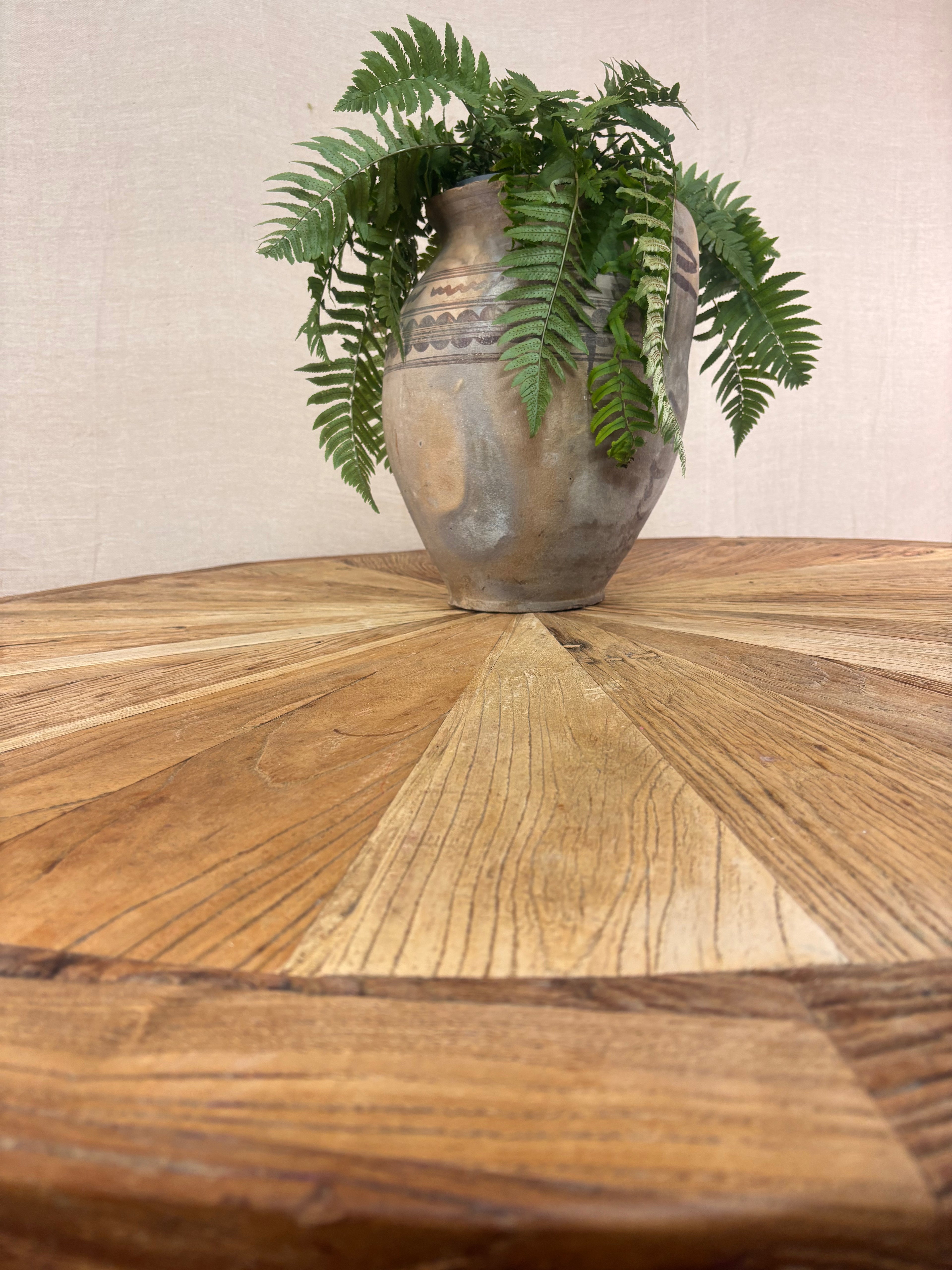 Rustic round wooden pedestal dining table with sunburst-patterned top and cross-leg base, photographed against a neutral backdrop.