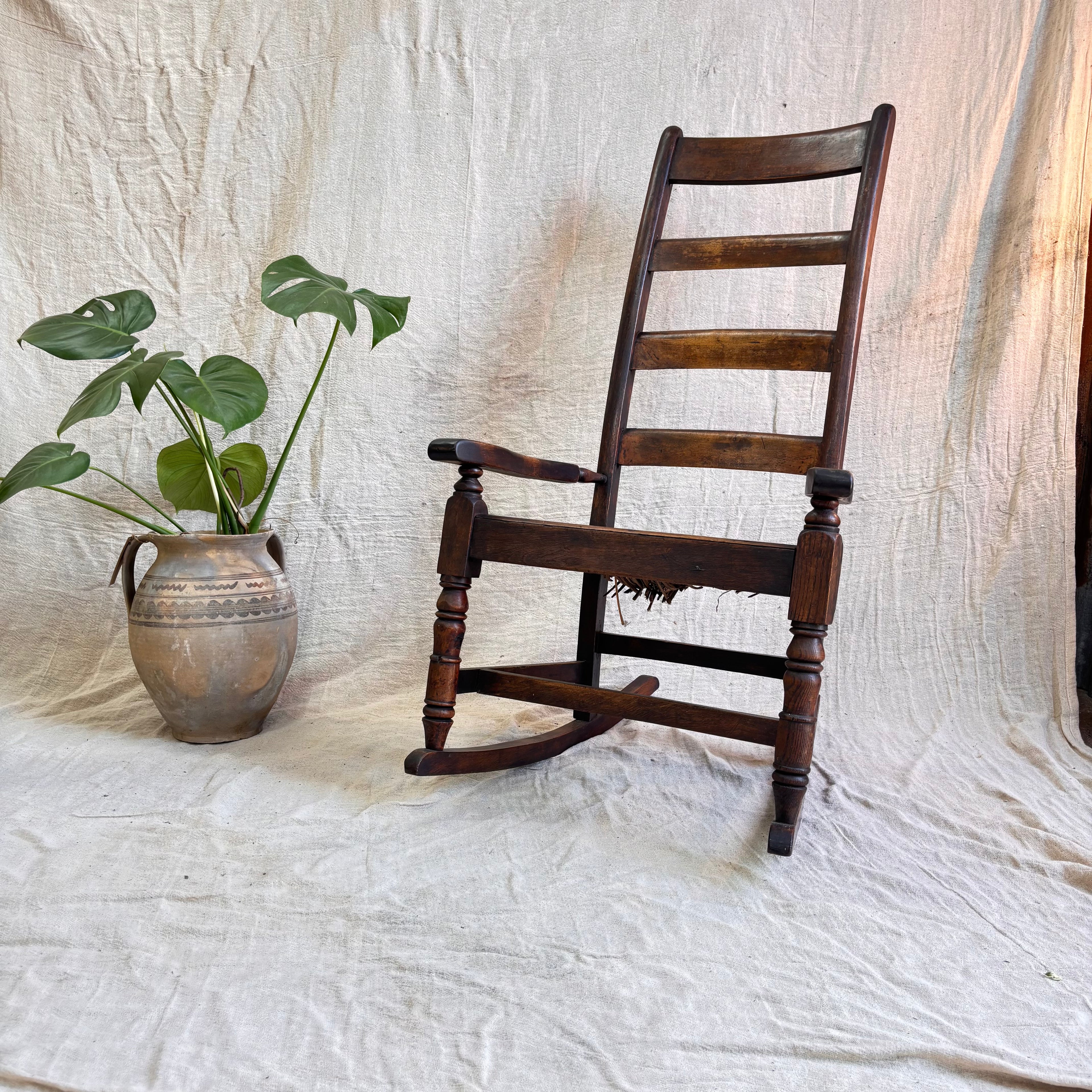 Wooden ladder-back chair next to a vase with green leaves on a textured white background