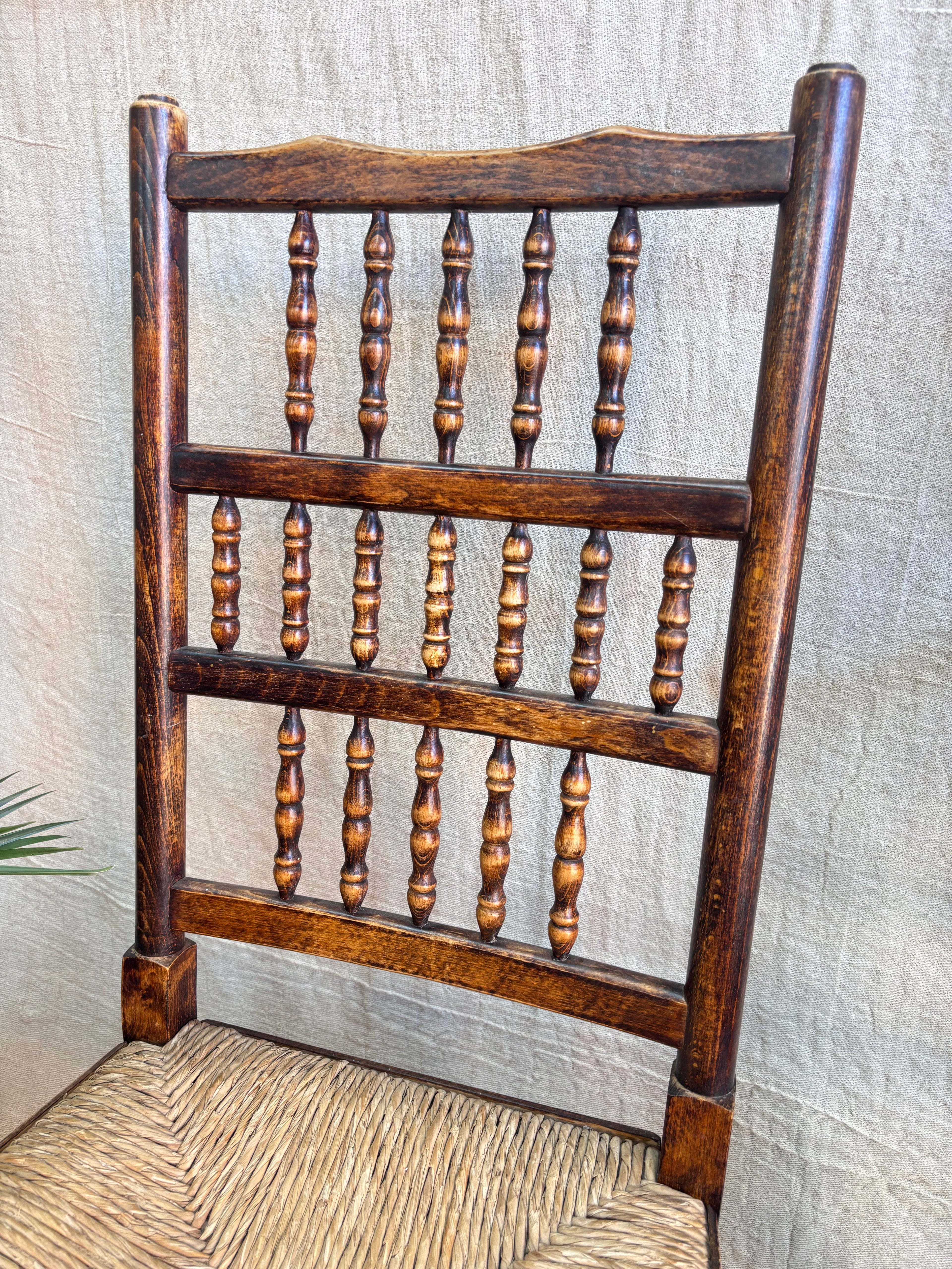 Wooden chair with woven seat and turned  backrest against a neutral background