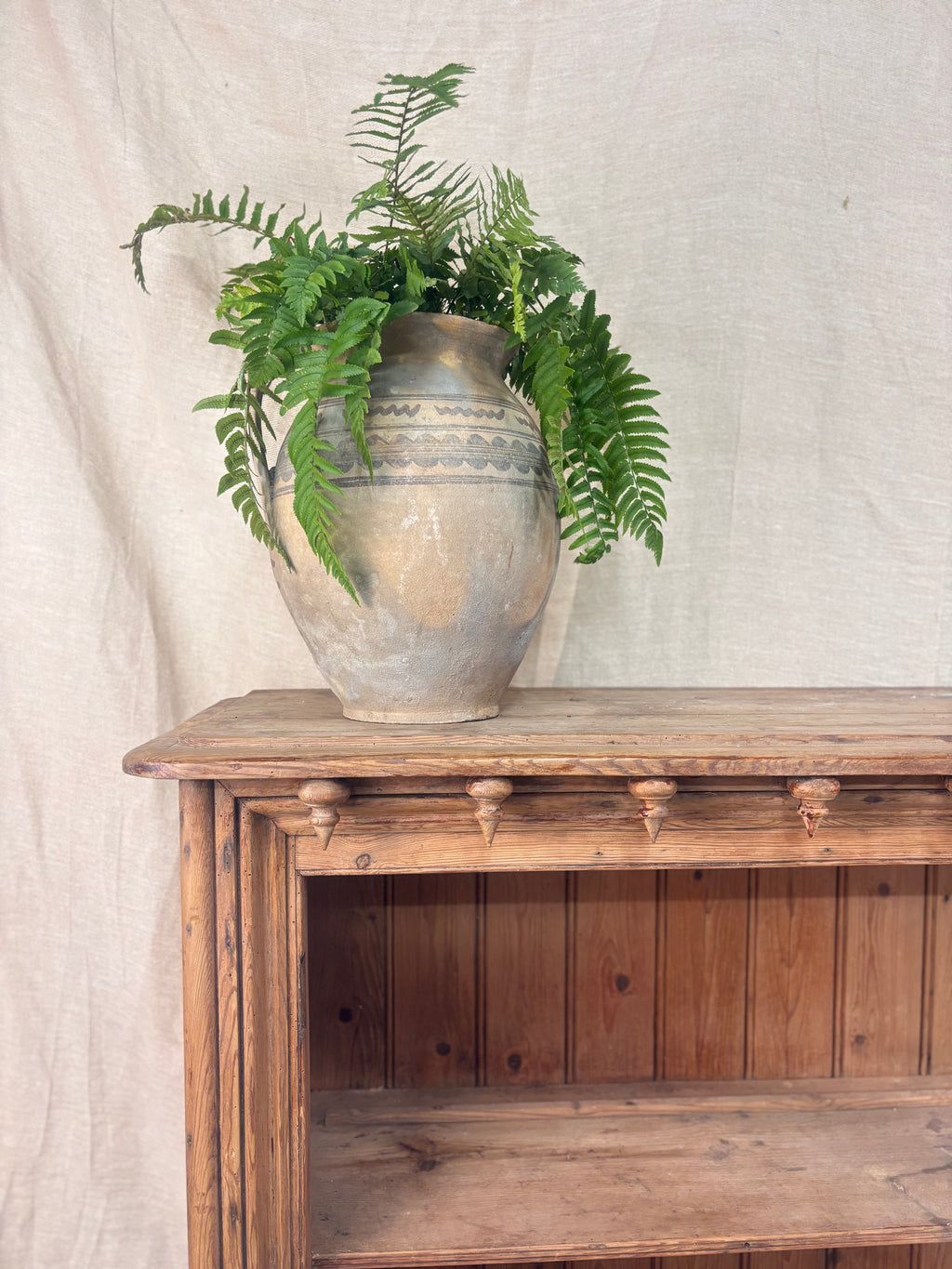 Vintage-style wooden bookcase with a large decorative vase and green ferns against a neutral background