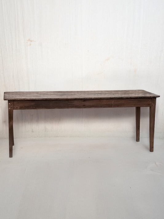 A rustic dark brown wooden dining table with a rectangular top and four legs, shown against a plain off-white wall.