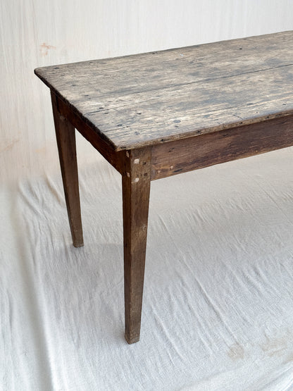 A rustic dark brown wooden table with a weathered, textured top and four legs, photographed against a white fabric backdrop.