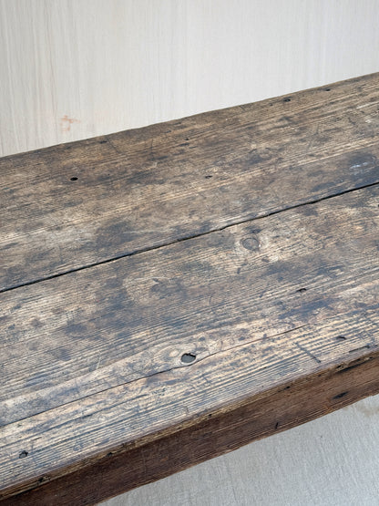 A close-up of a rustic dark brown wooden plank surface with visible grain, knots, and weathered texture against a light neutral background.