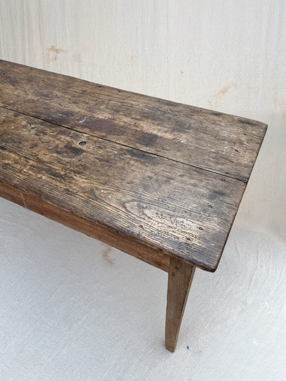 A rustic dark brown wooden bench with a weathered, hand-scraped finish and visible grain, shown against a light off-white textured background.