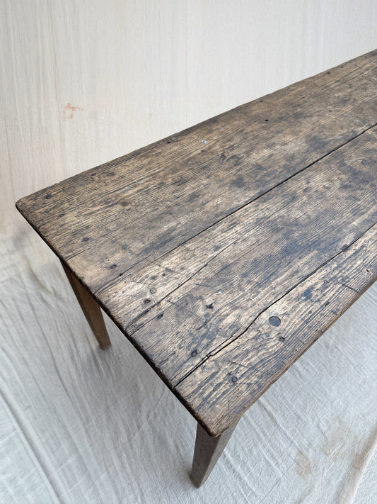 A rustic rectangular wooden bench or table made from weathered dark brown planks, photographed against a light fabric backdrop.