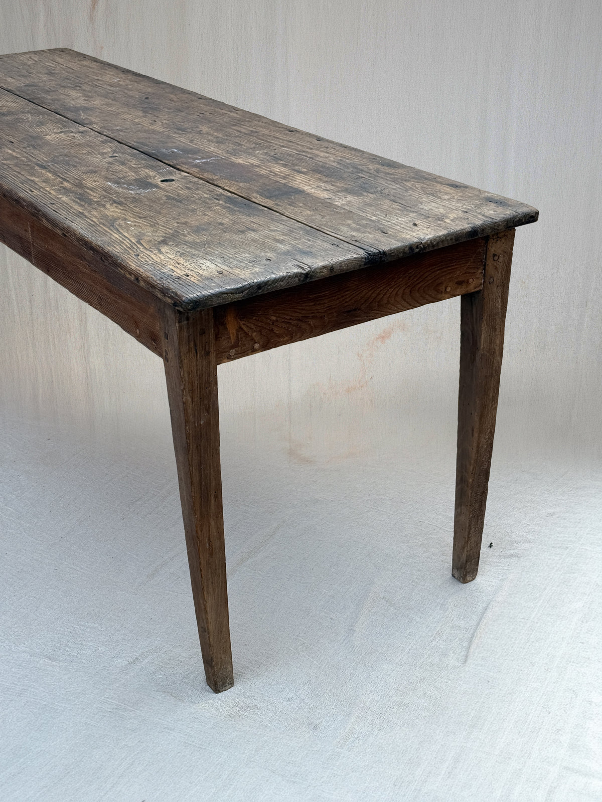 A rustic dark wood table with a weathered, aged finish and four legs, photographed against a light gray fabric backdrop.