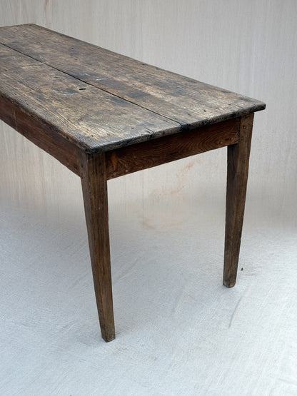 A rustic dark wood table with a weathered, aged finish and four legs, photographed against a light gray fabric backdrop.