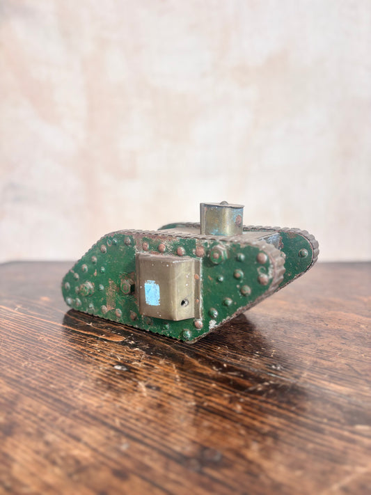 A vintage green metal tank toy or model with rivets and a small blue accent, resting on a rustic wooden table against a textured beige background.