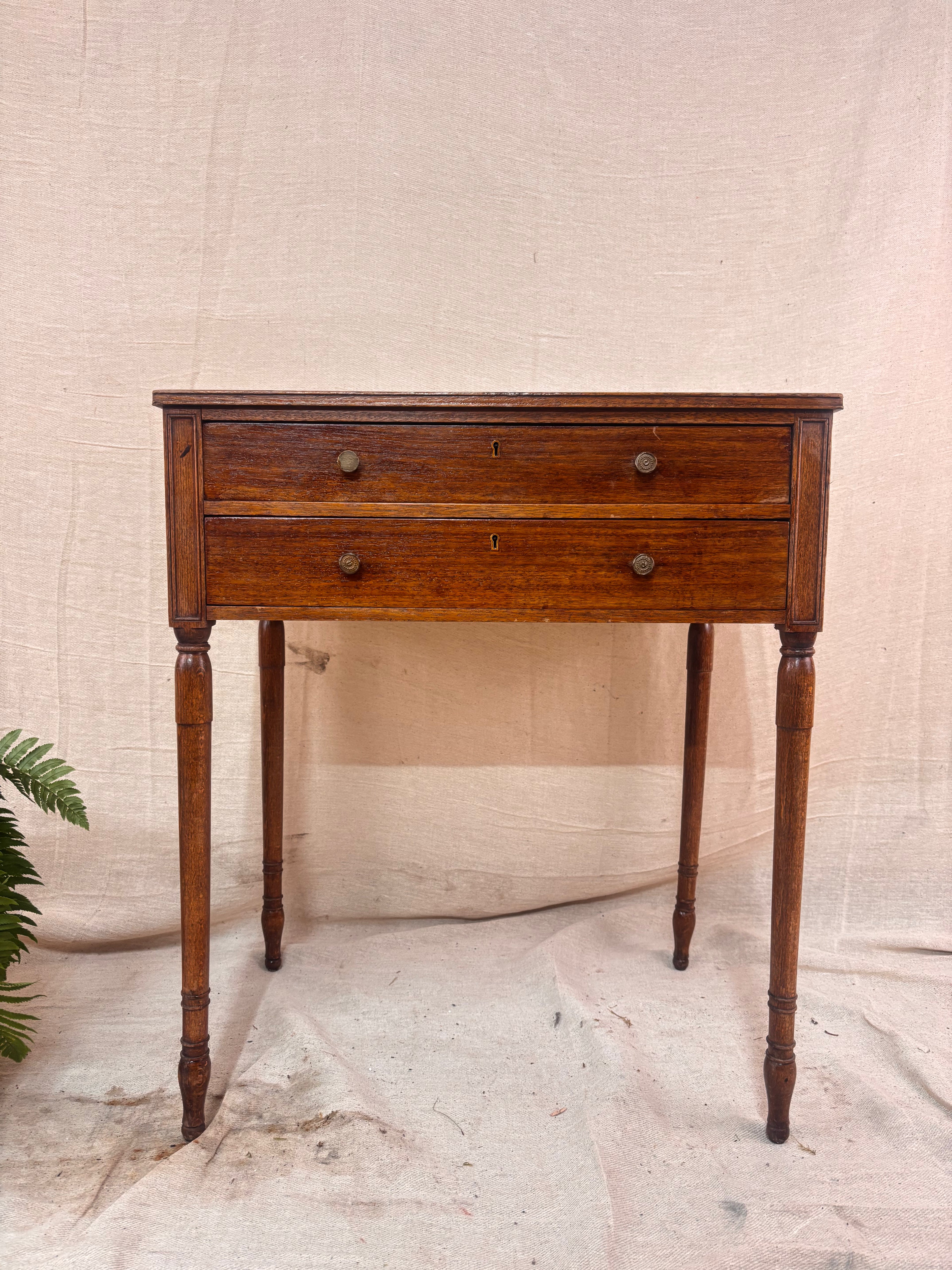 Regency-style mahogany side table with two drawers, slender ring-turned legs, and a neo-classical design, shown on a neutral background.