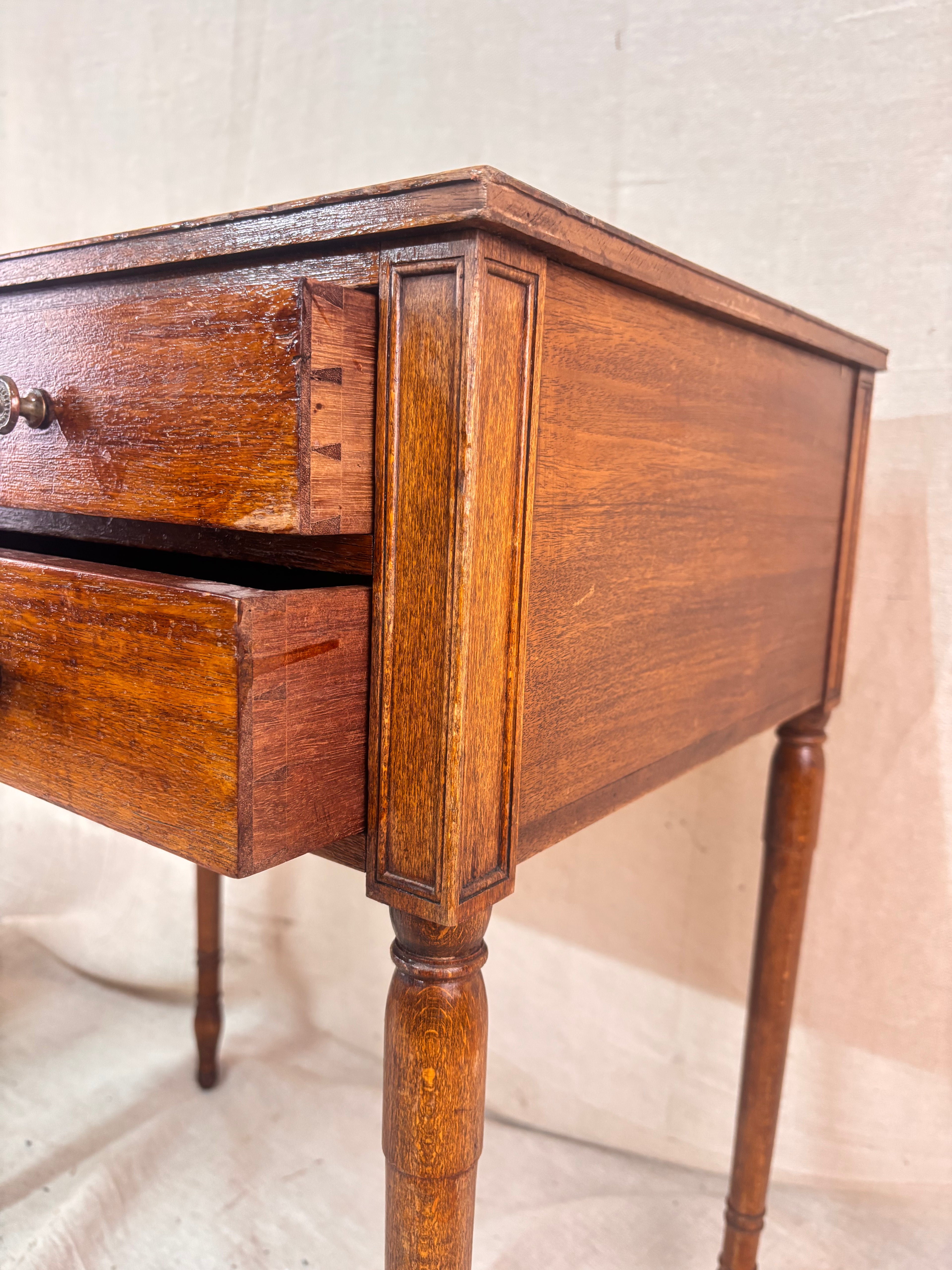 Regency-style mahogany side table with two drawers, slender ring-turned legs, and a neo-classical design, shown on a neutral background.