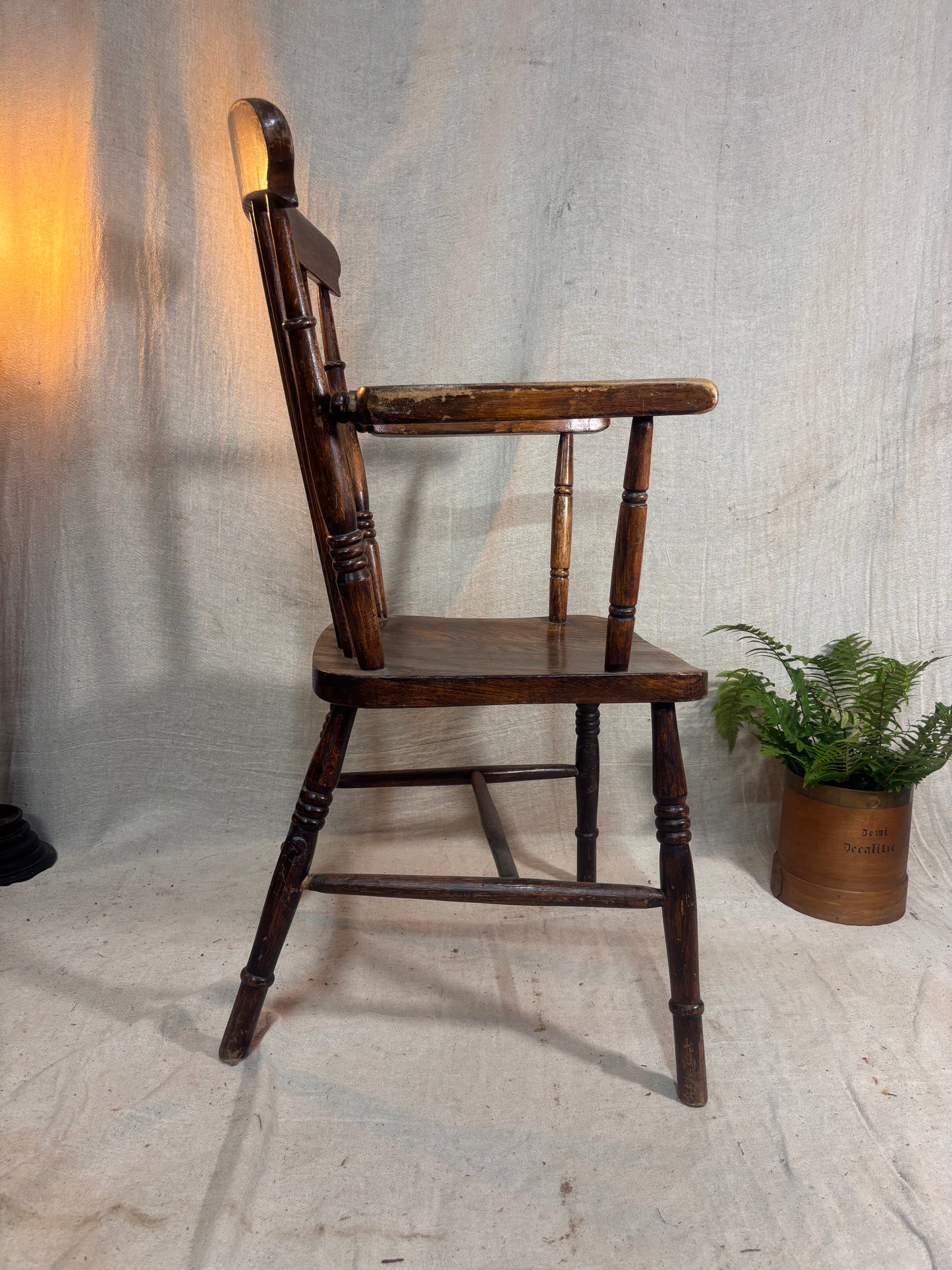 Wooden chair with armrests against a textured wall with a plant in the corner.