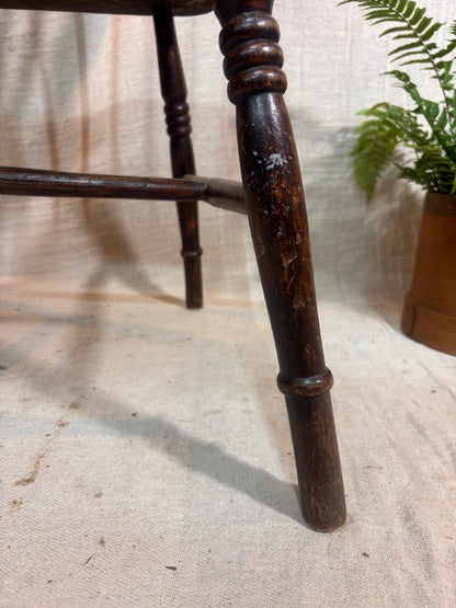 Close-up of a wooden chair leg on a textured surface with a plant in the background