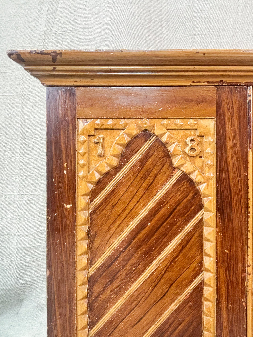 Wooden cabinet with intricate carvings and a decorative pattern on a textured wall background