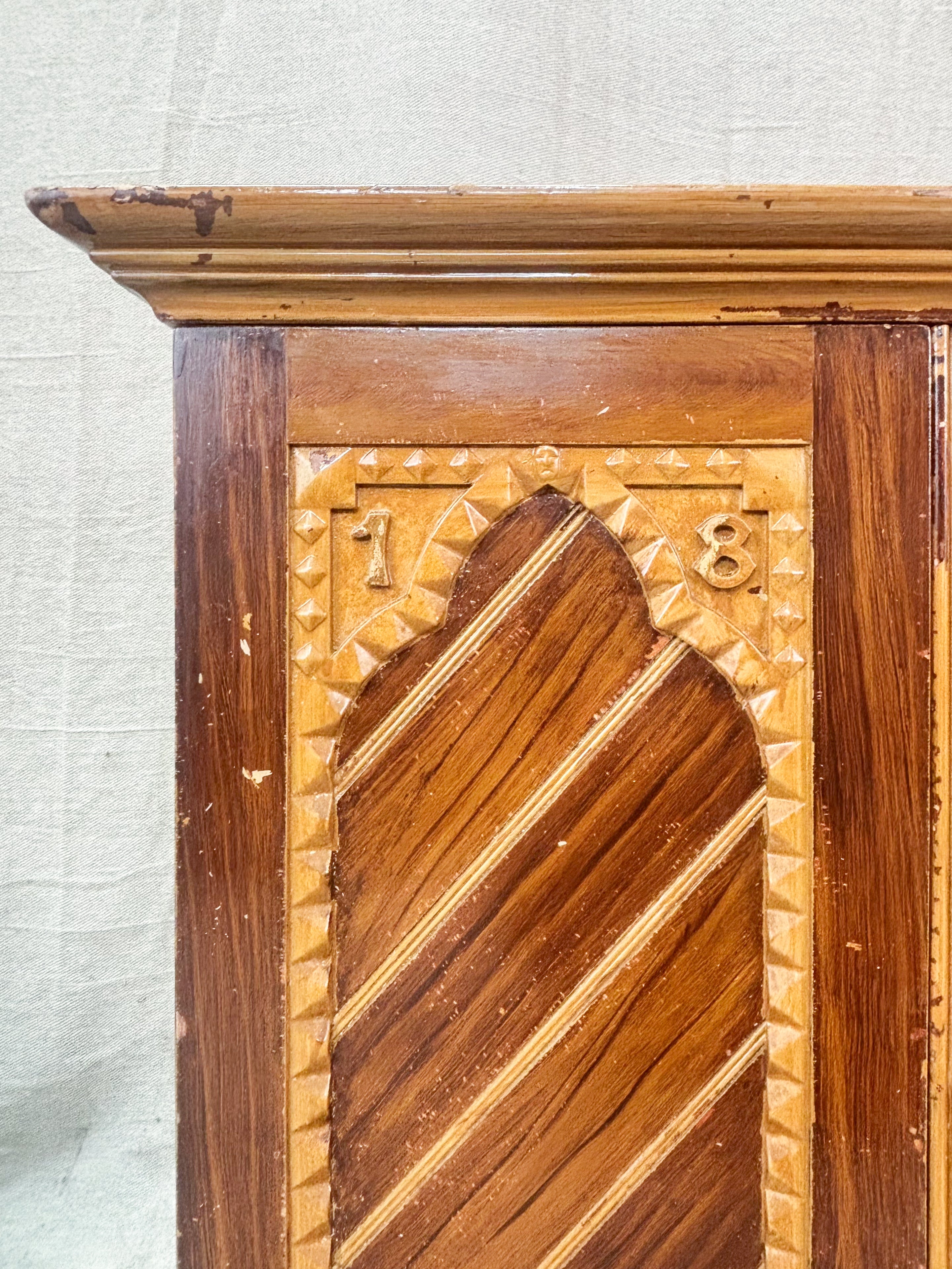 Wooden cabinet with intricate carvings and a decorative pattern on a textured wall background