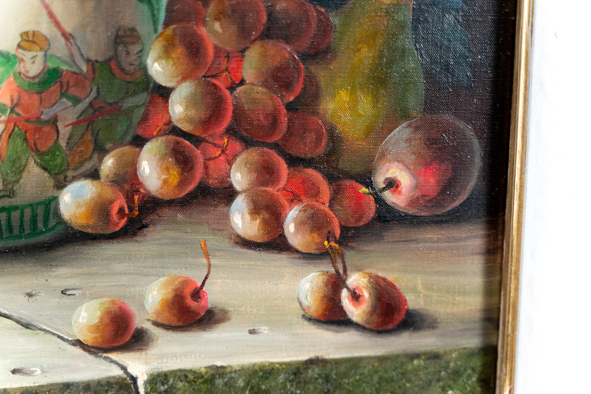 A close-up of a still life painting depicting a cluster of red and brown grapes, a pear, and a few scattered cherries on a tabletop, with part of a colorful decorative plate and a gold-toned frame visible.