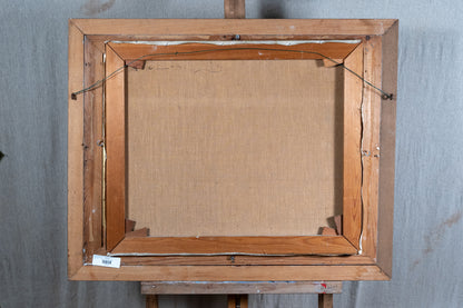 The back view of a framed canvas painting on an easel, showing the wooden frame, canvas backing, and hanging wires against a gray backdrop.