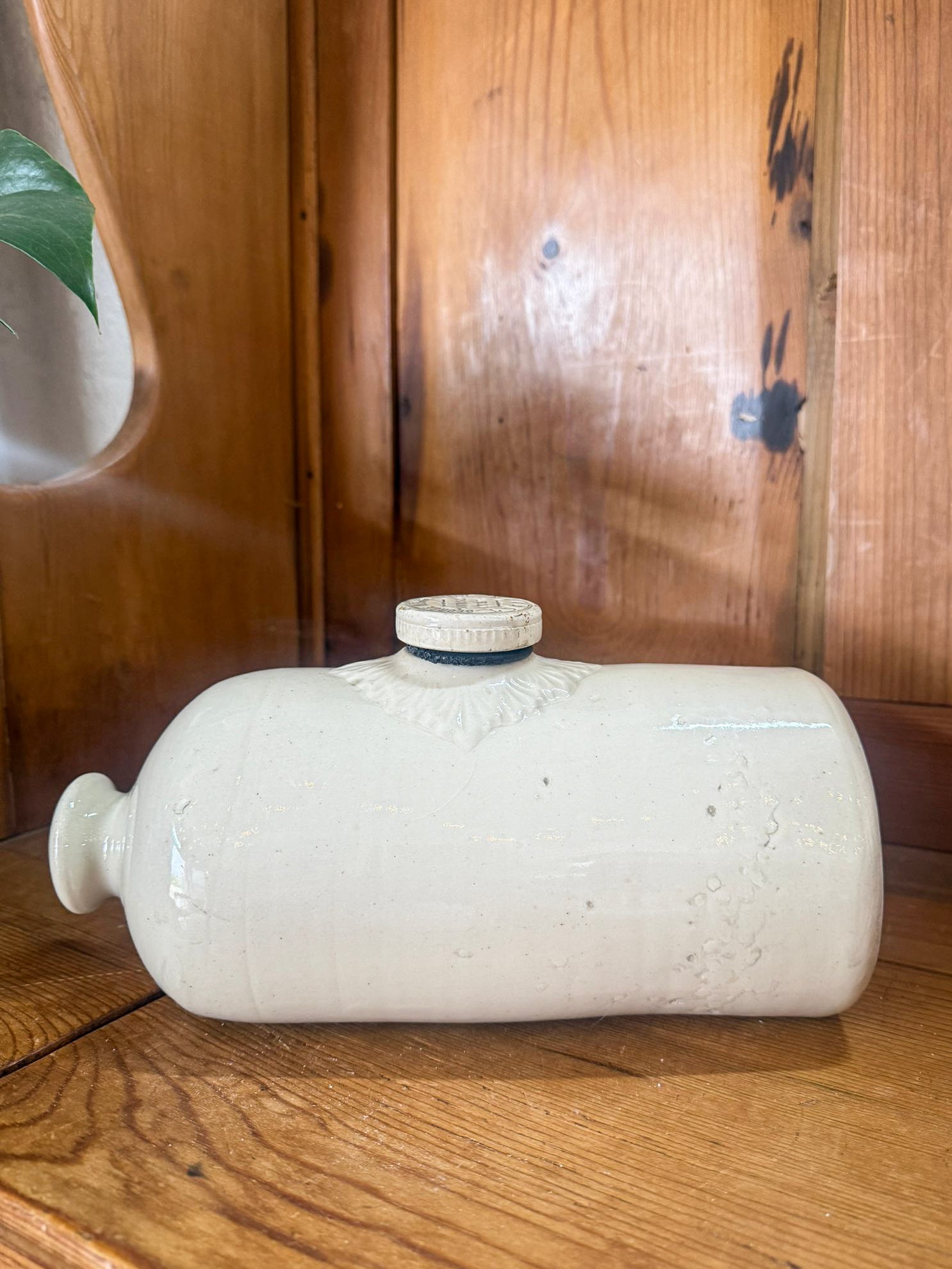 White stoneware hot water bottle on a wooden surface with a wooden cabinet in the background