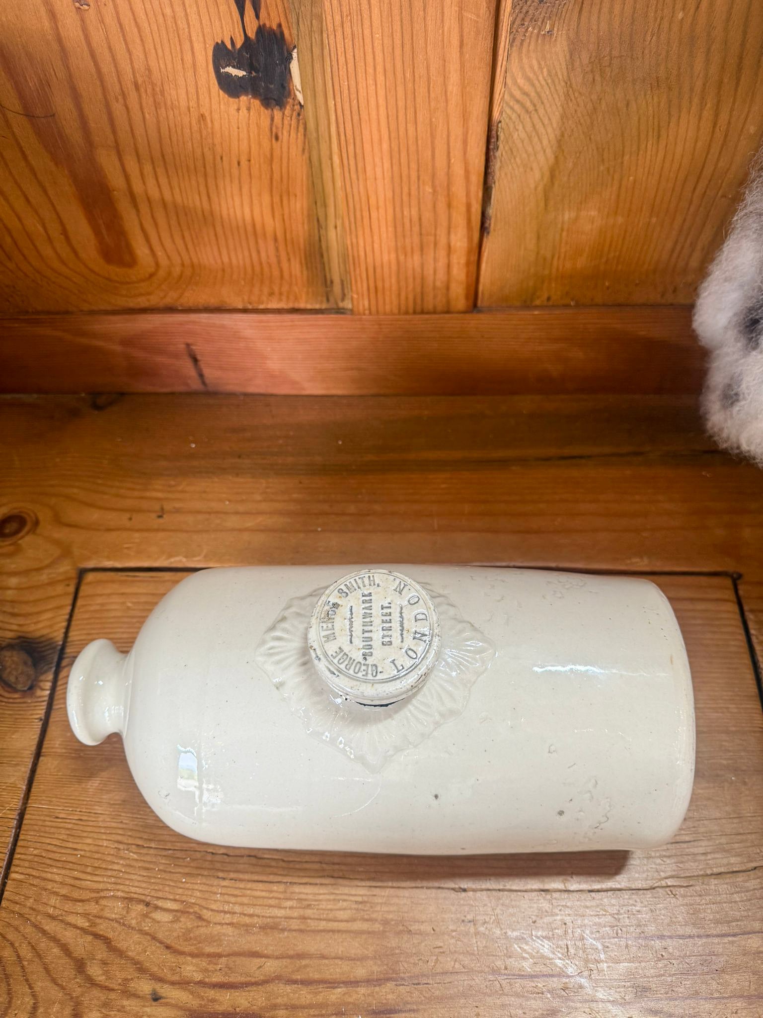 stoneware hot water bottle with a label on a wooden floor