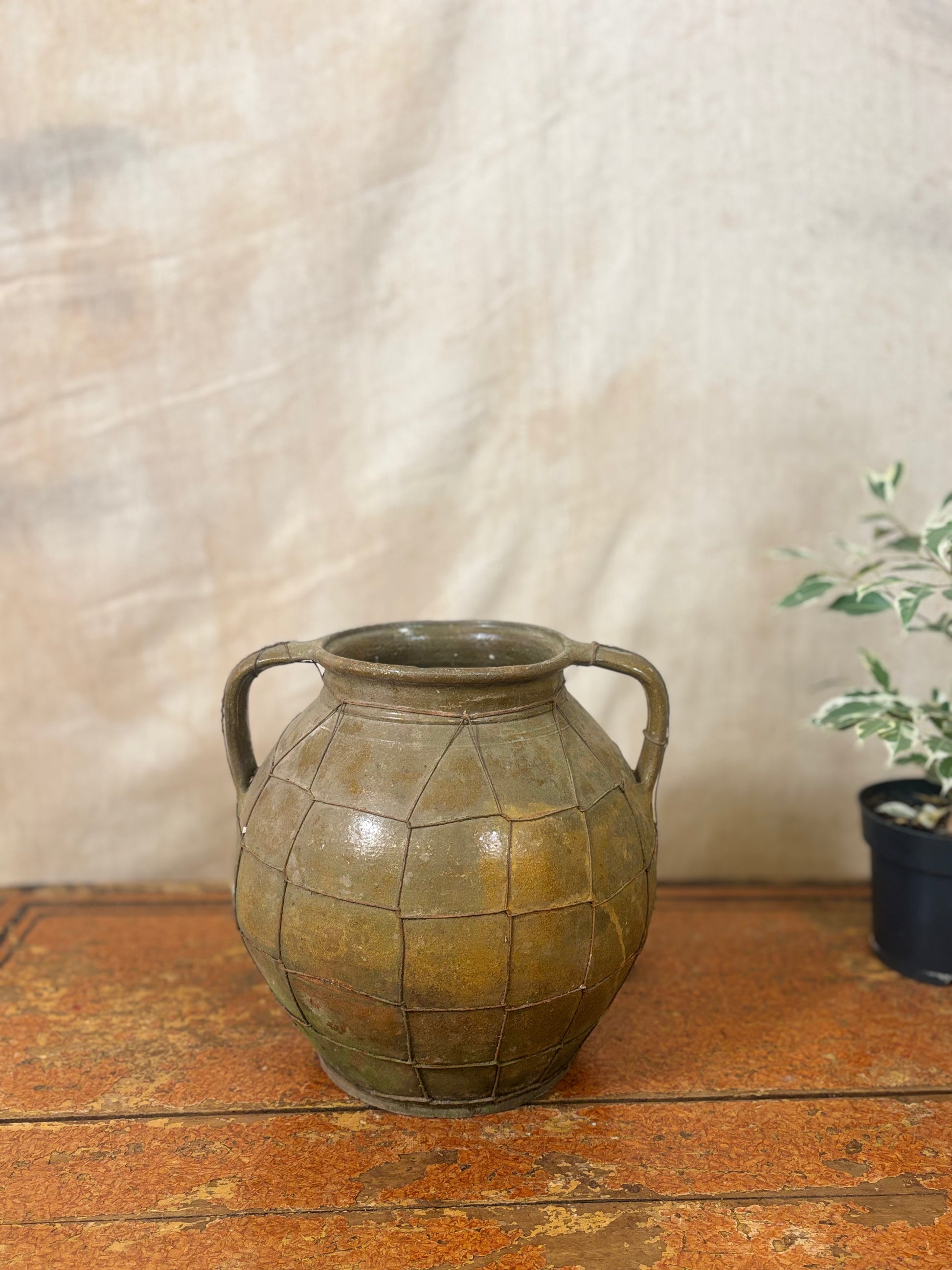 Vintage-style green ceramic vase with grid pattern on a wooden surface