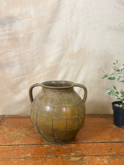 Vintage-style green ceramic vase with grid pattern on a wooden surface