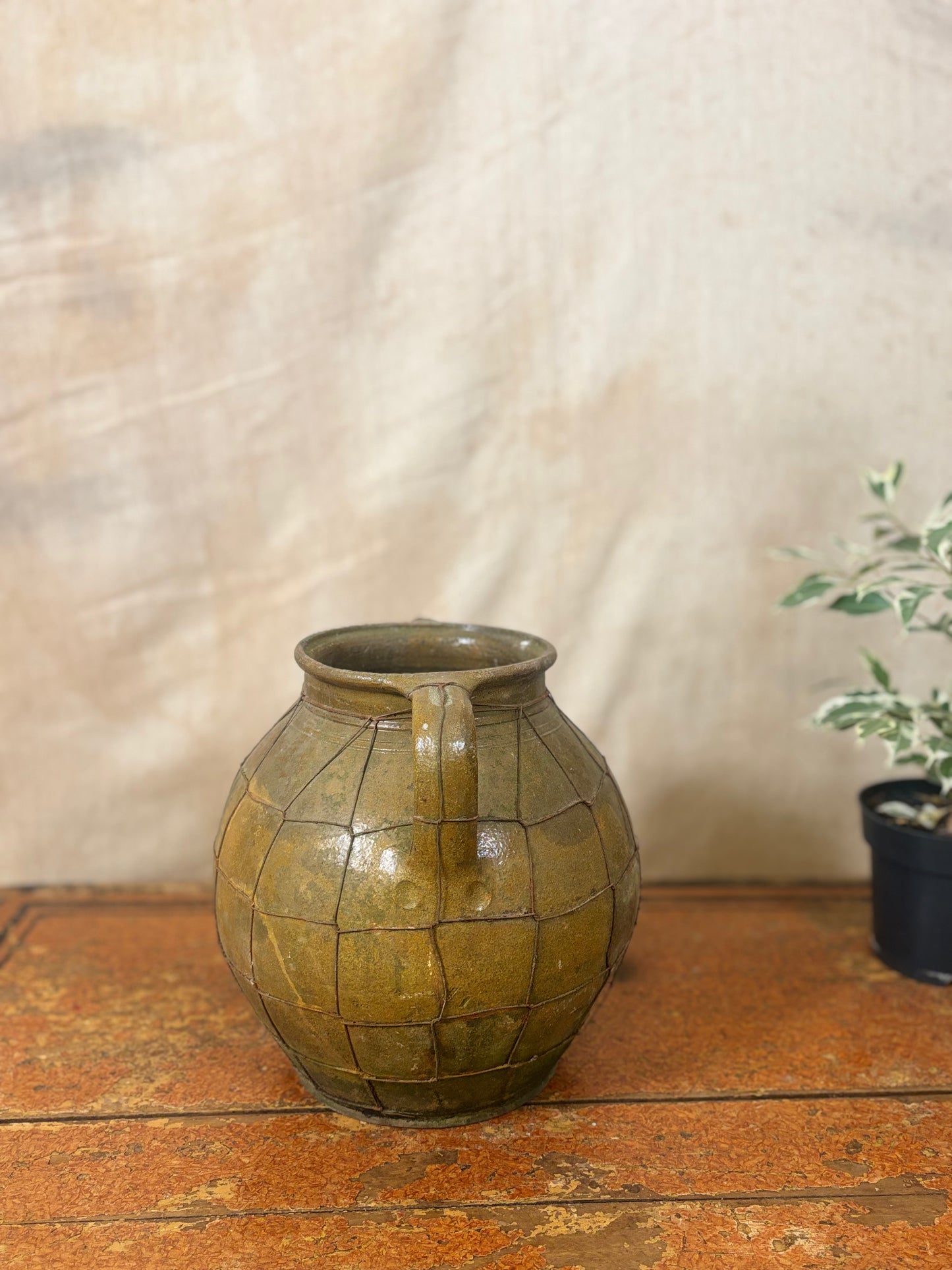 Vintage green ceramic jar with a textured surface on a wooden surface.