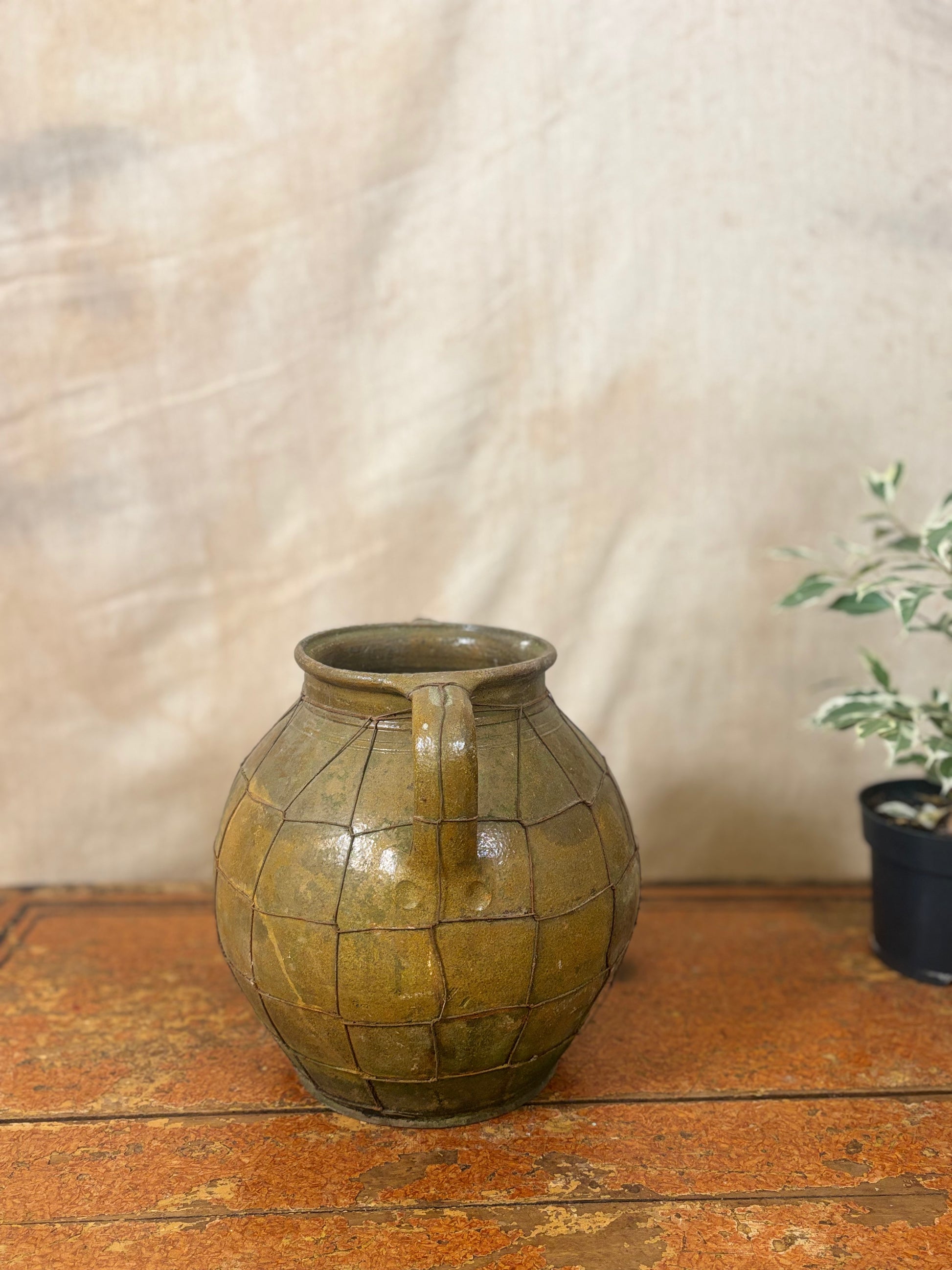 Vintage green ceramic jar with a textured surface on a wooden surface.